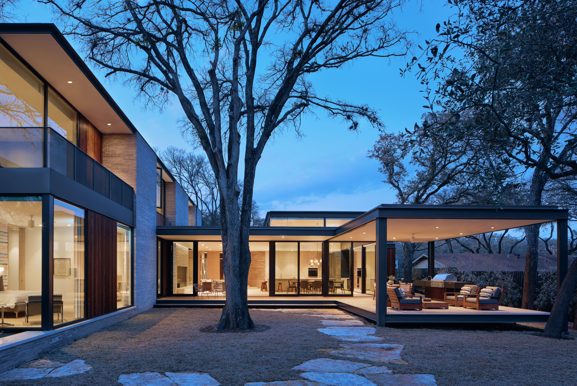 Courtyard view at dusk with three glazed volumes arranged around a preserved oak tree