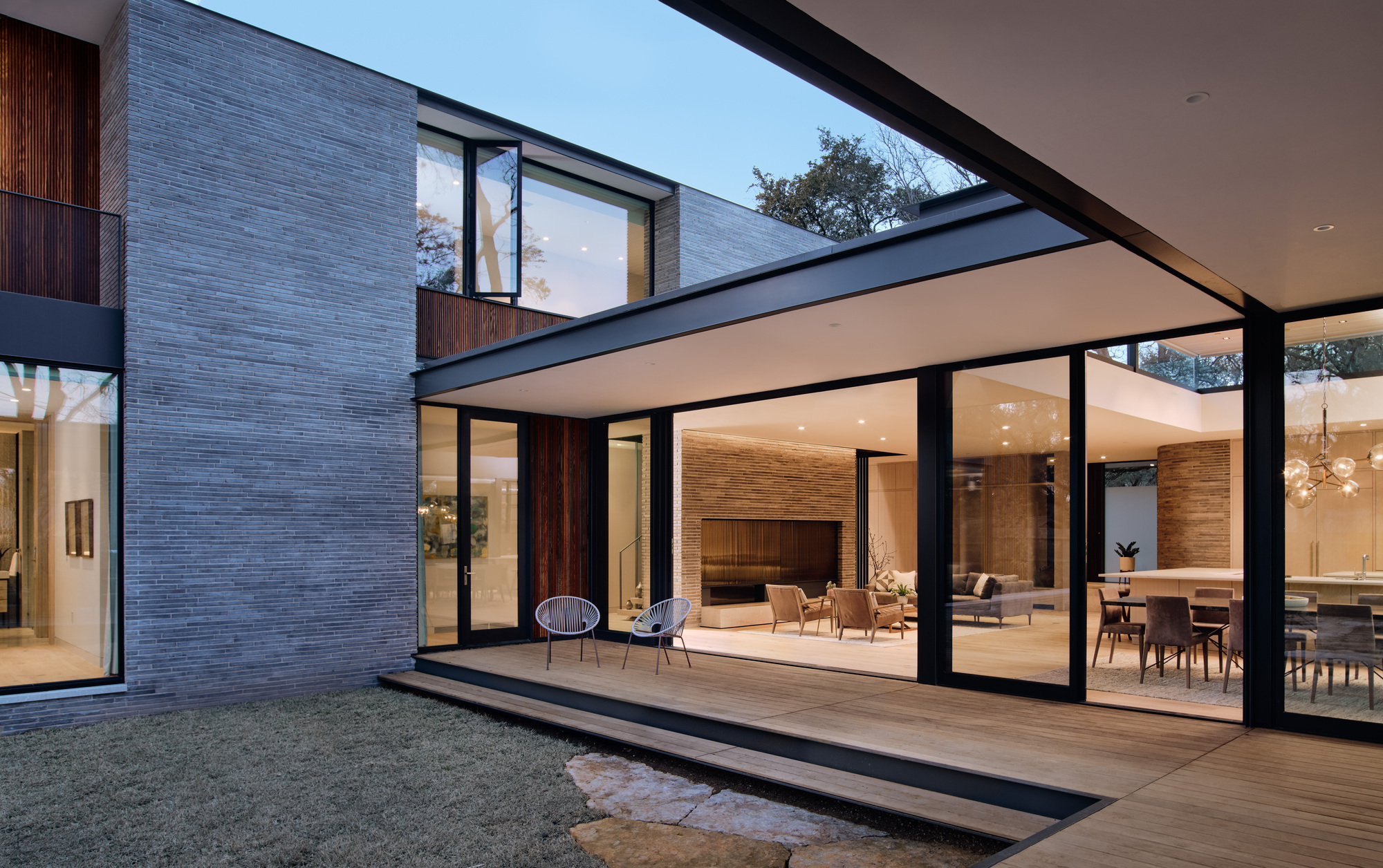 Courtyard view of the glass-walled living space framed by black steel beams at dusk