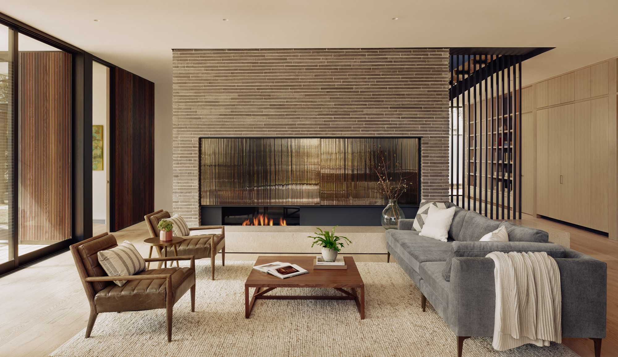Living room with horizontal brick fireplace wall and vertical slat screen beside floor-to-ceiling glazing
