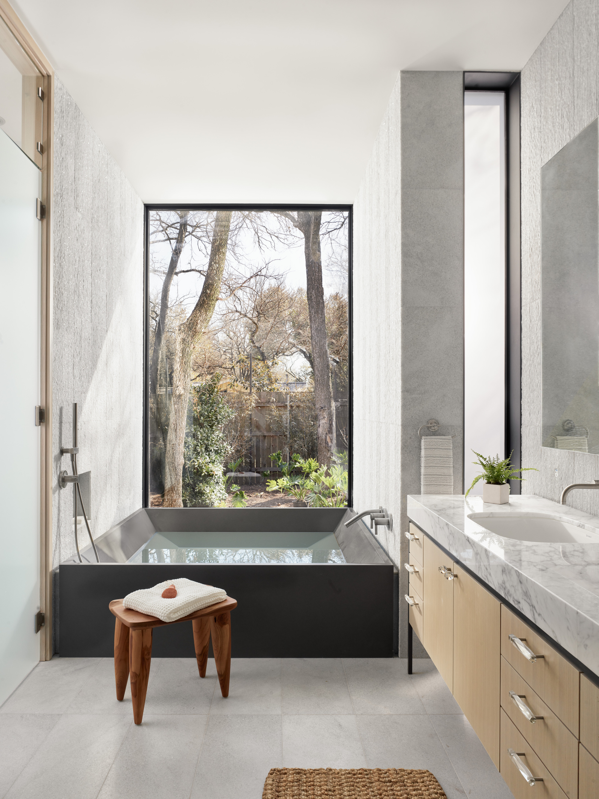 Bathroom with black soaking tub positioned beneath a tall window framing bare trees outside