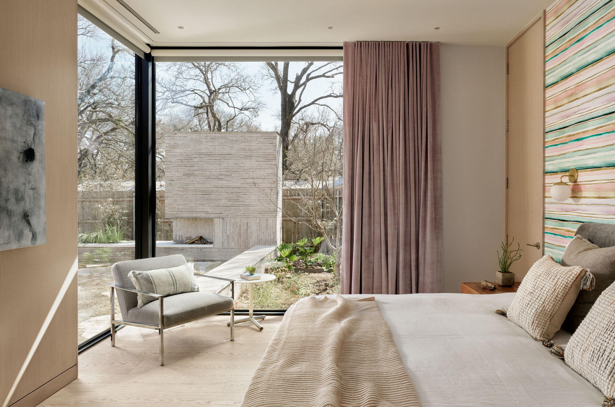 Bedroom with full-height glazing overlooking a courtyard garden under winter light