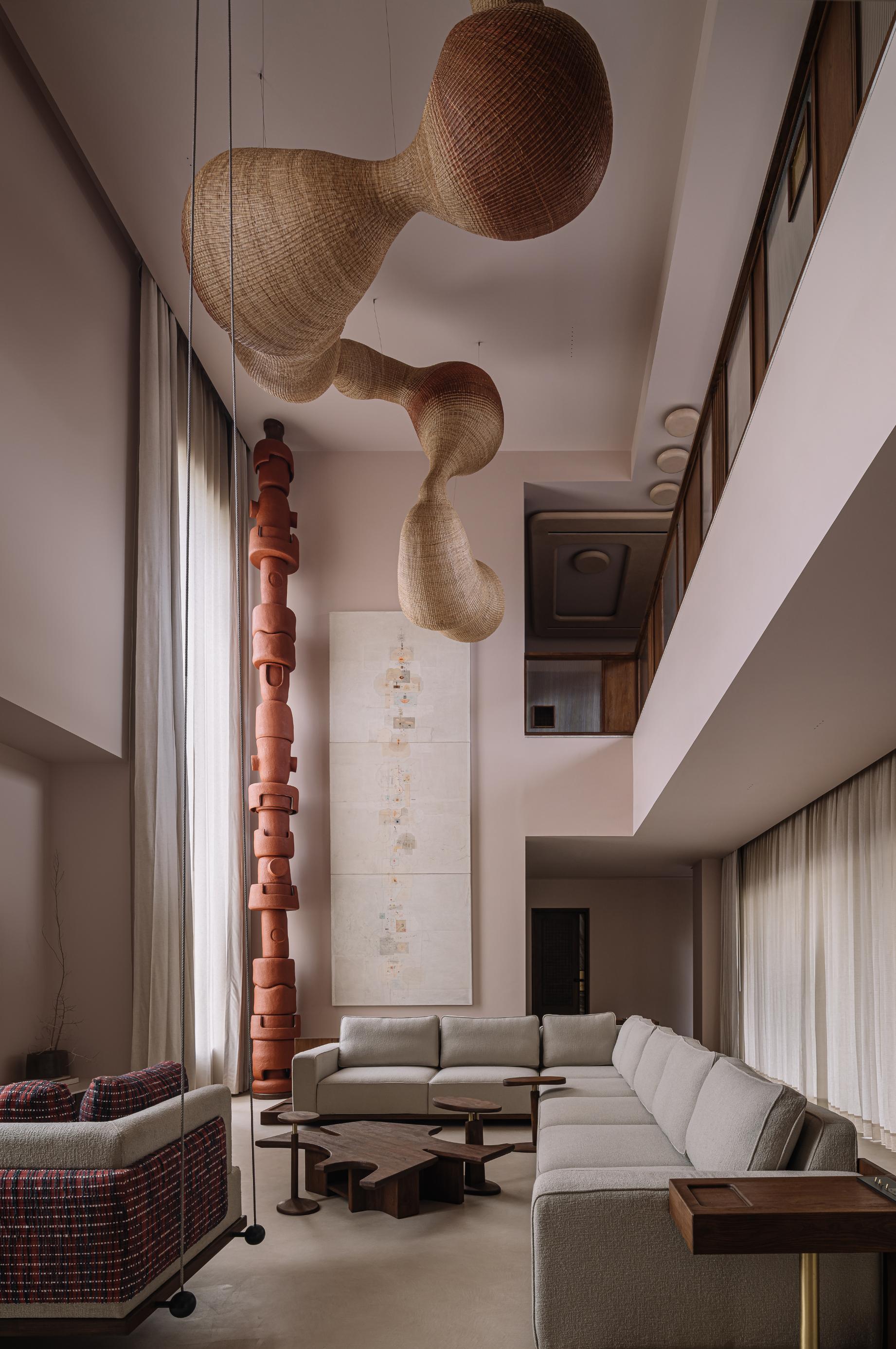 Double-height living space with woven pendant lights and a sculptural terracotta column beside sectional seating