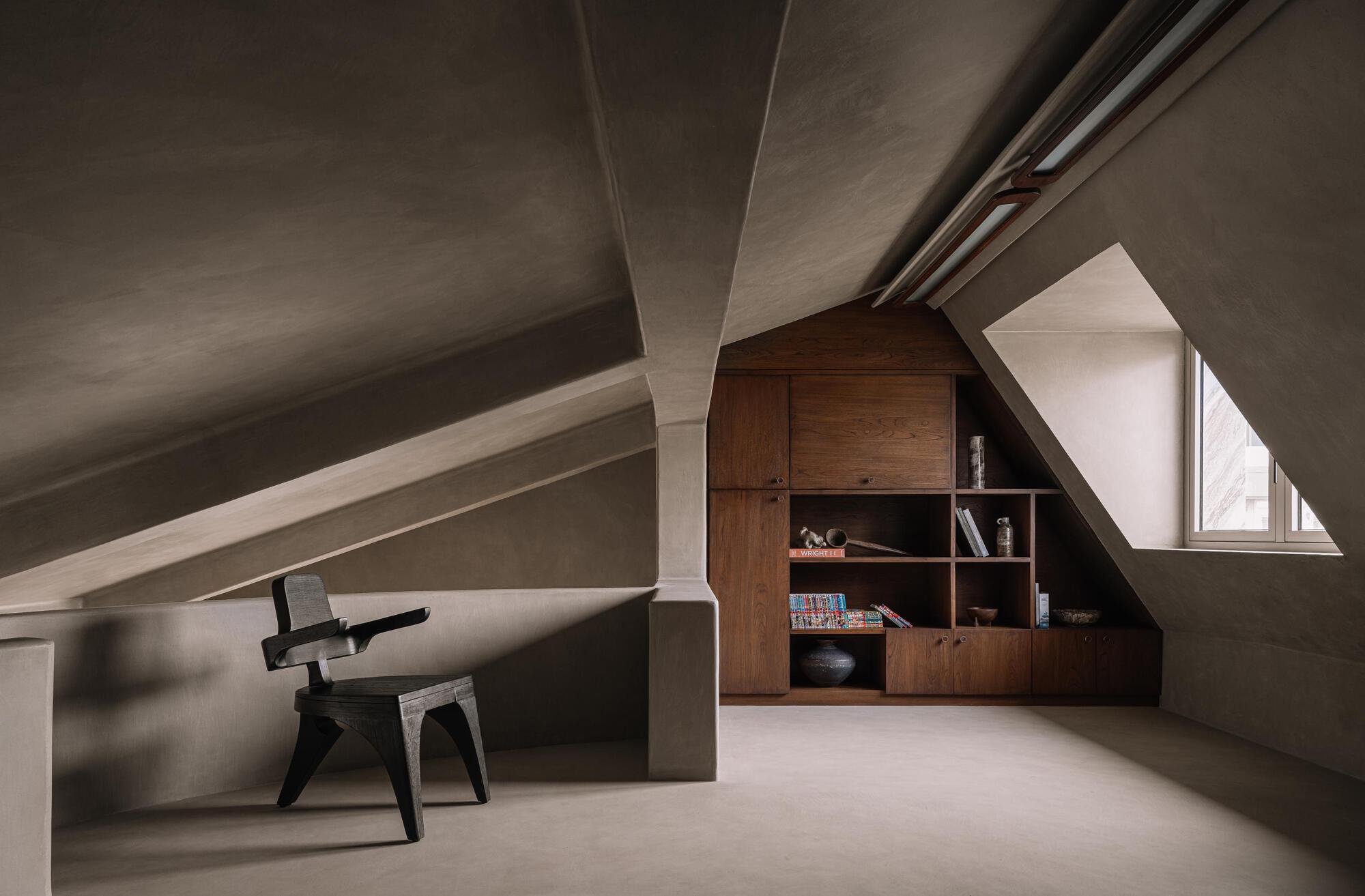 Attic workspace with exposed pitched ceiling beams and a built-in timber bookshelf under a triangular window