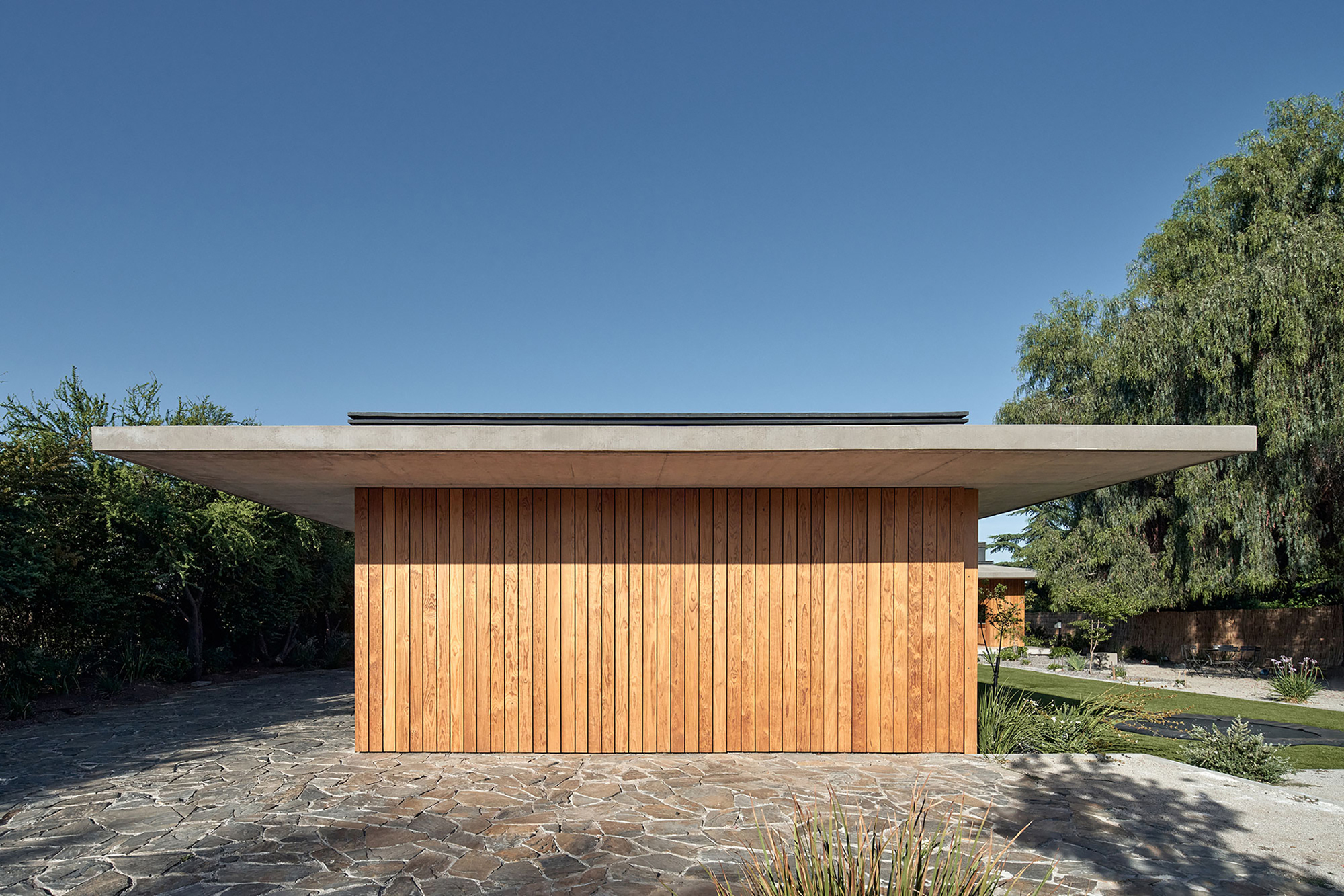 Street facade with vertical timber cladding under a broad concrete roof on a clear day