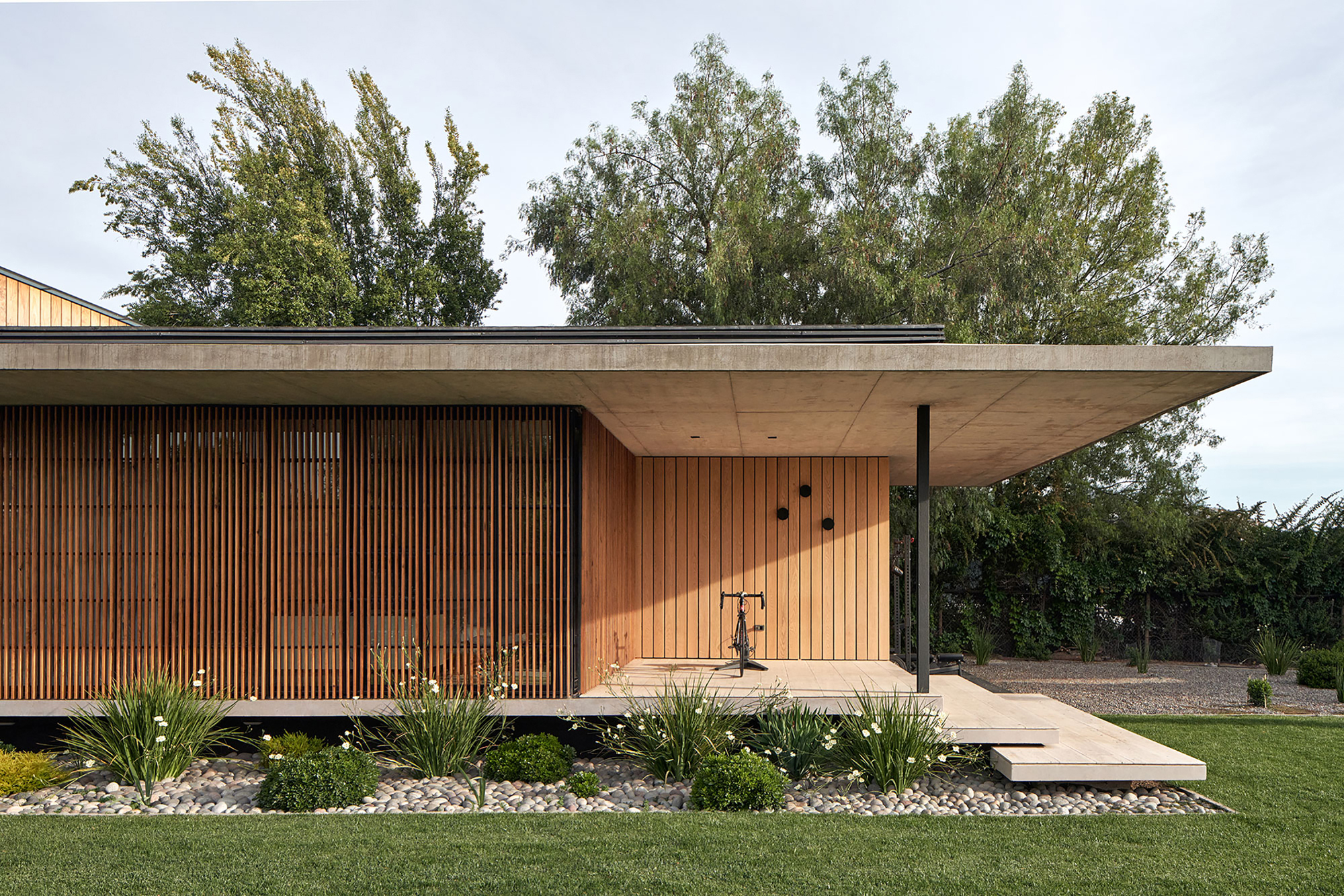 Garden facade with vertical timber screens and gravel planting bed beneath mature trees