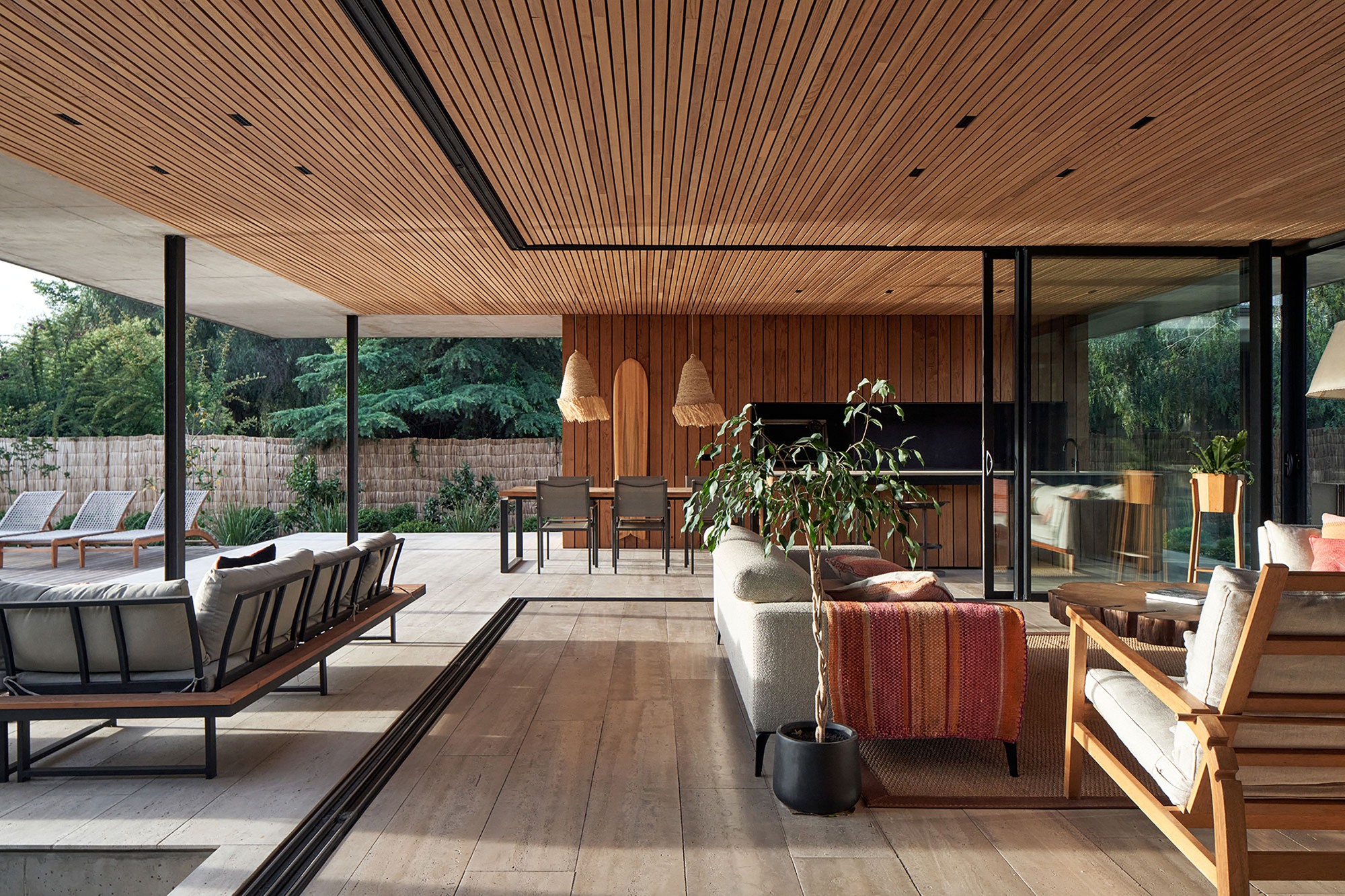 Open plan living space with timber slat ceiling and glazed walls facing the pool deck