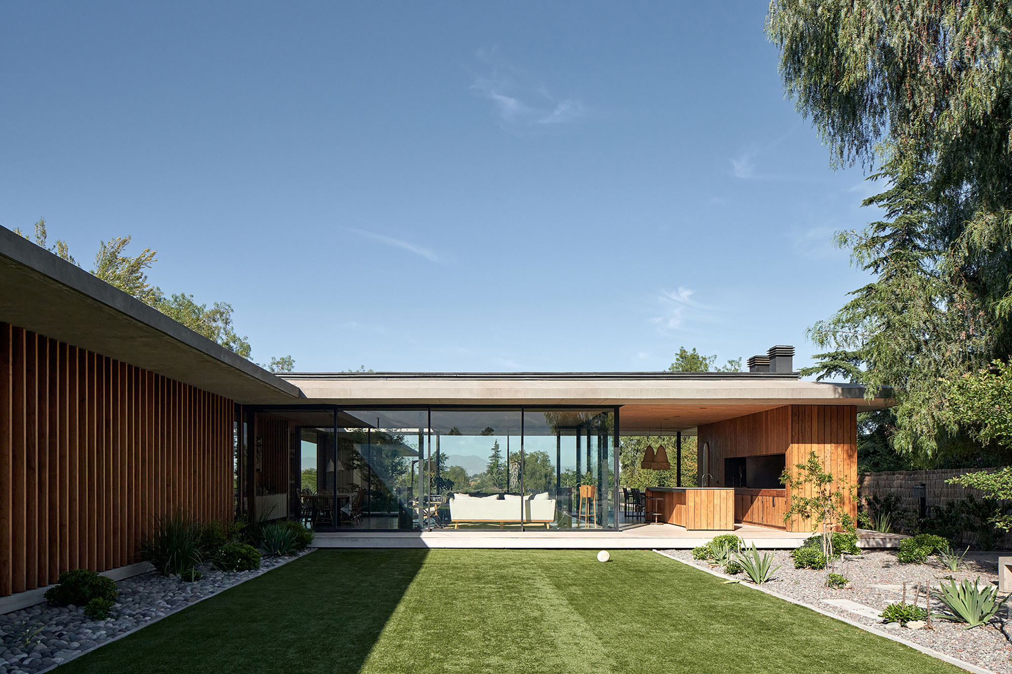 Garden view showing the continuous flat roof spanning timber clad volumes and glazed corners