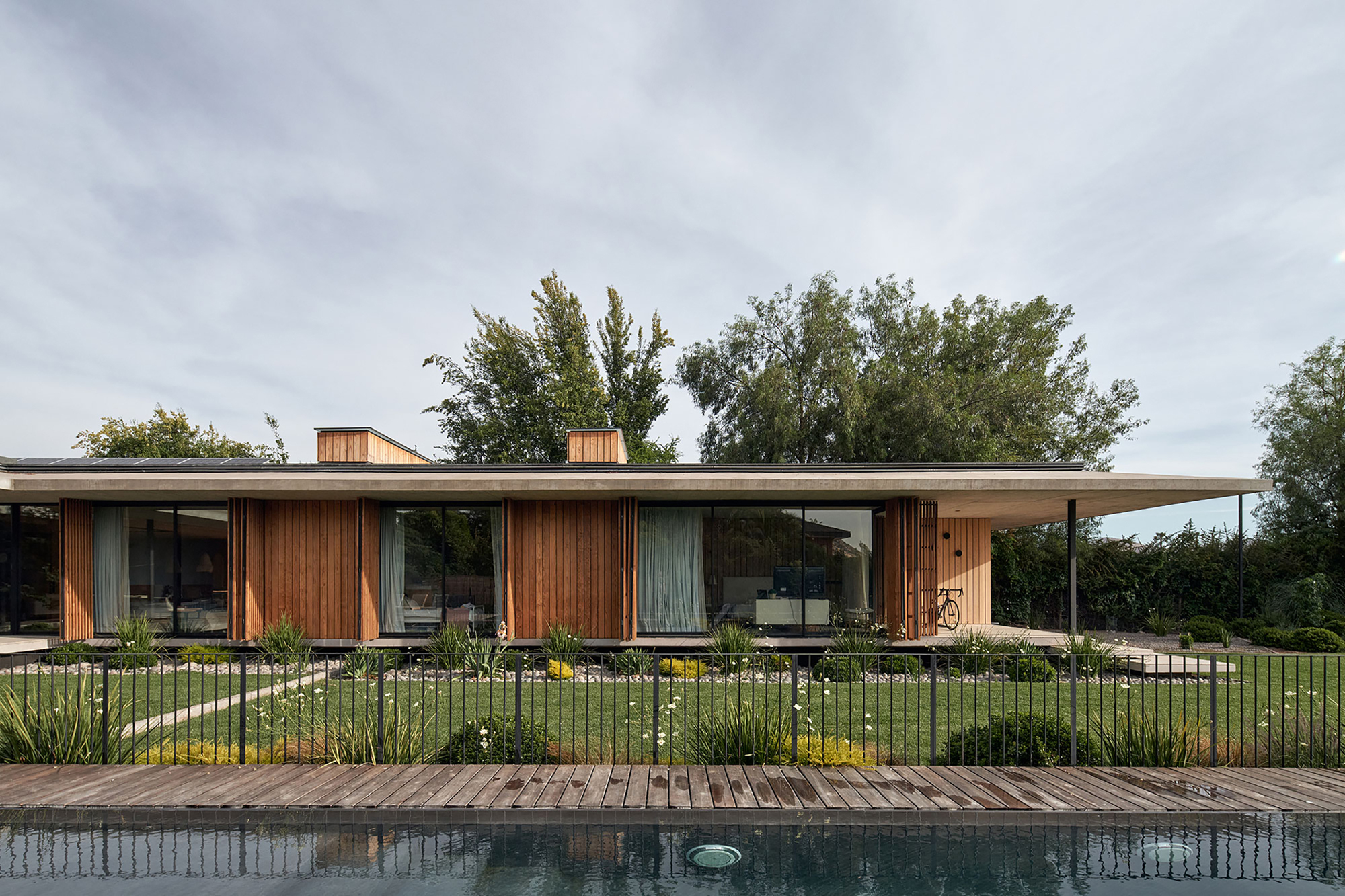 Garden facade with timber screen panels and glazing above timber pool deck and planted buffer