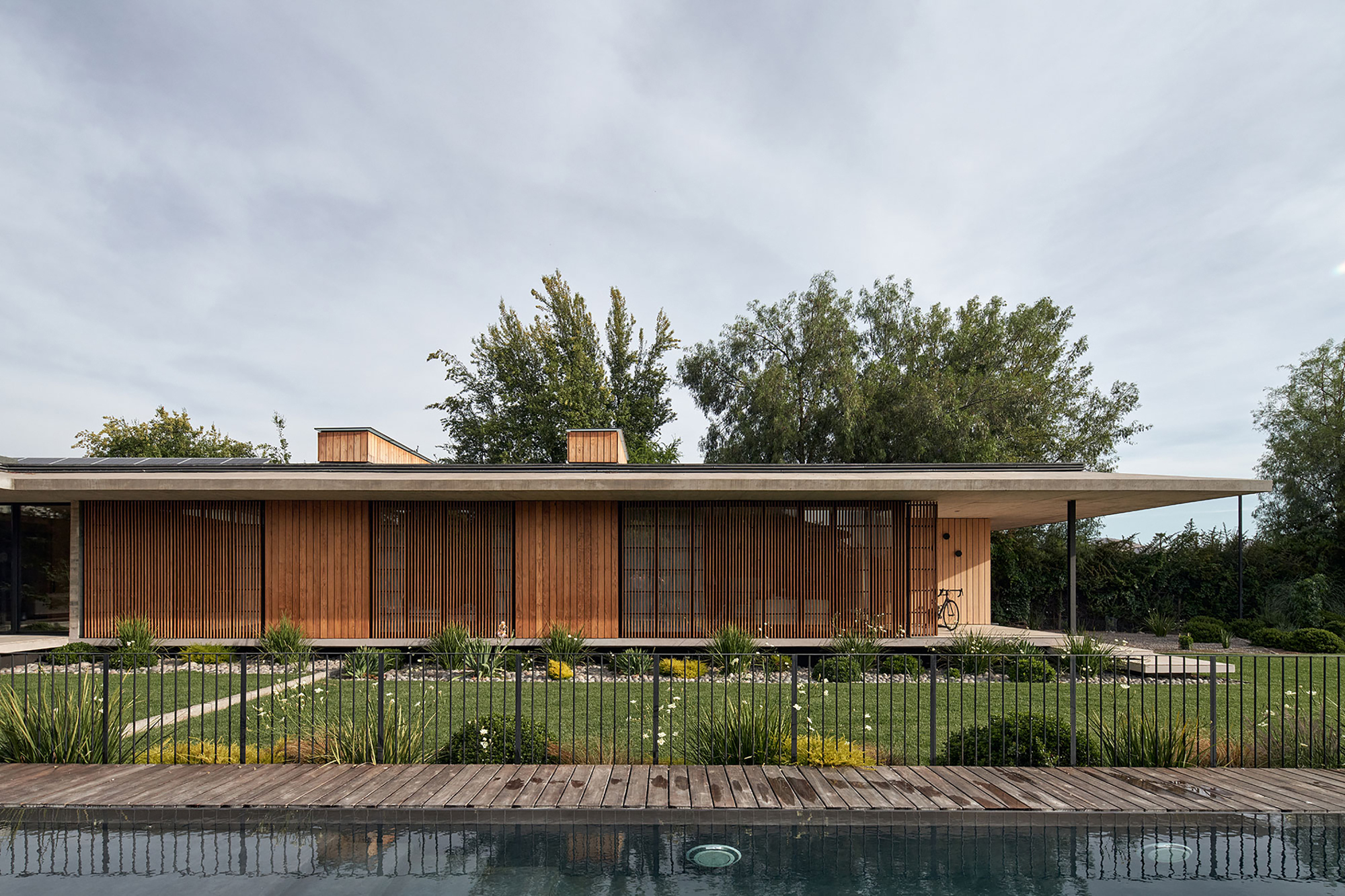 Poolside elevation showing sliding timber screens and continuous roof plane under overcast sky