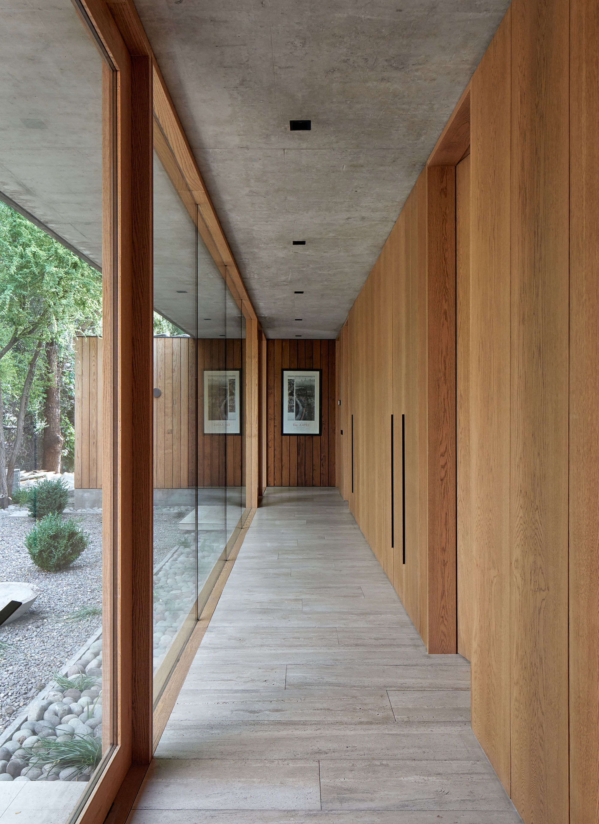 Corridor with board-formed concrete ceiling, timber-framed glazing and oak storage wall beside pale timber flooring