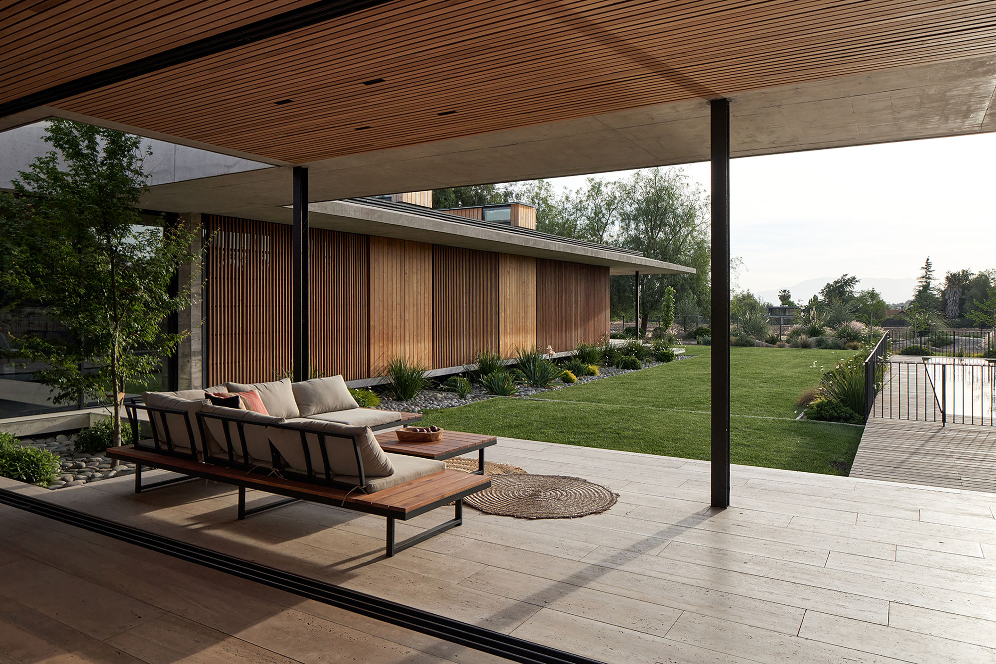 Covered terrace with timber slat ceiling and outdoor seating overlooking lawn at dusk