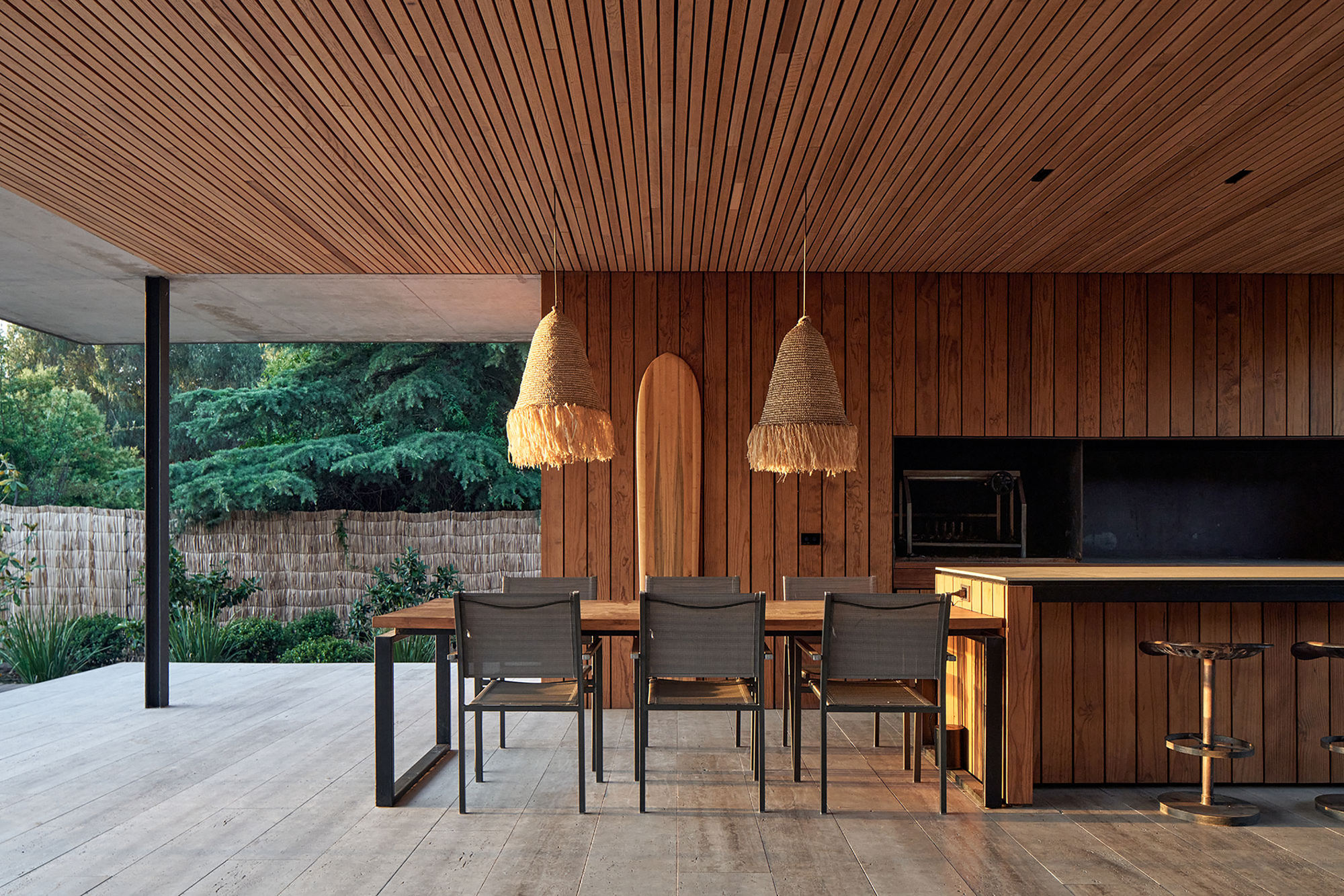 Dining area with timber walls and woven pendant lights opening to a covered terrace at dusk