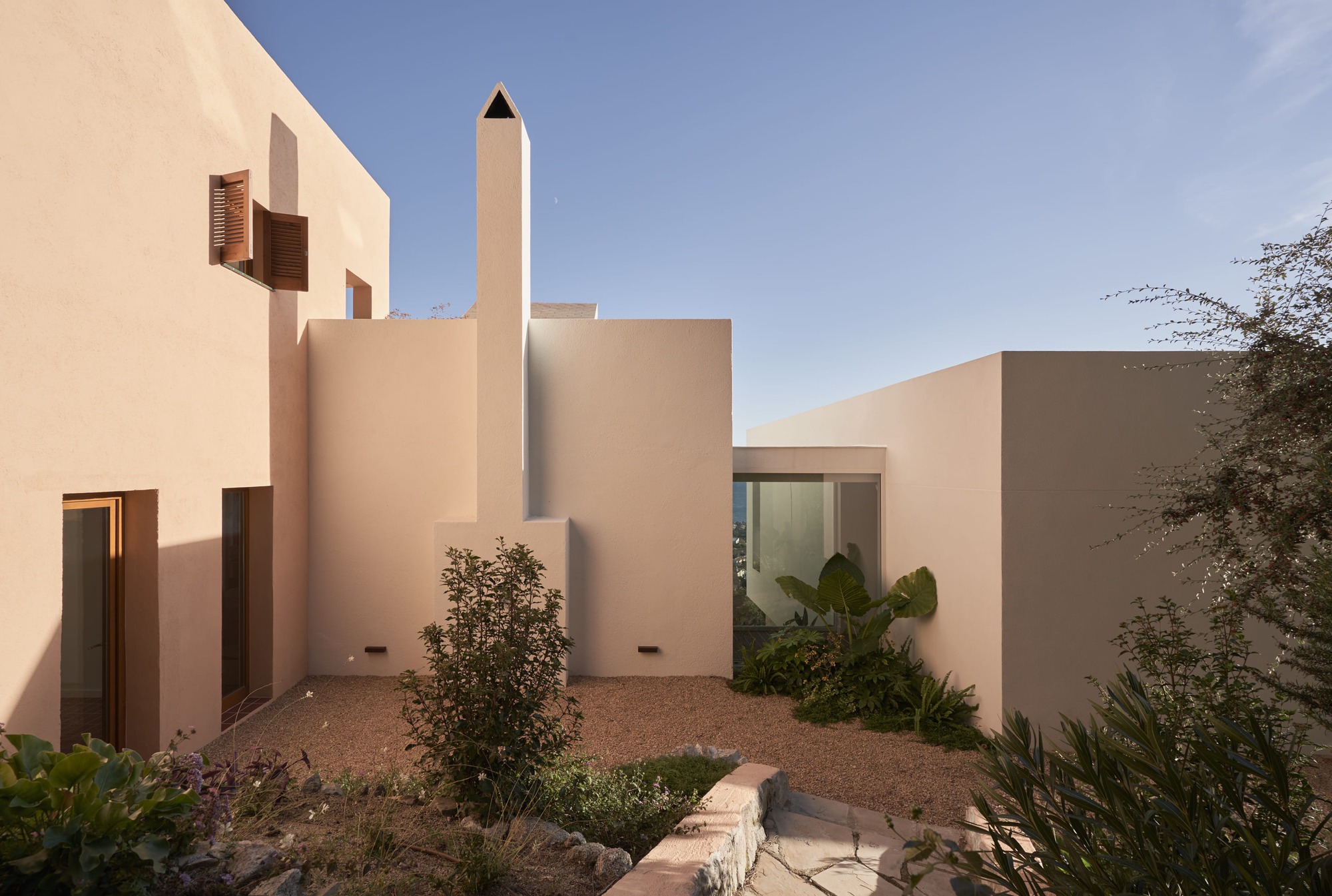 Courtyard with tall cylindrical chimney rising above clustered stucco volumes with desert plantings