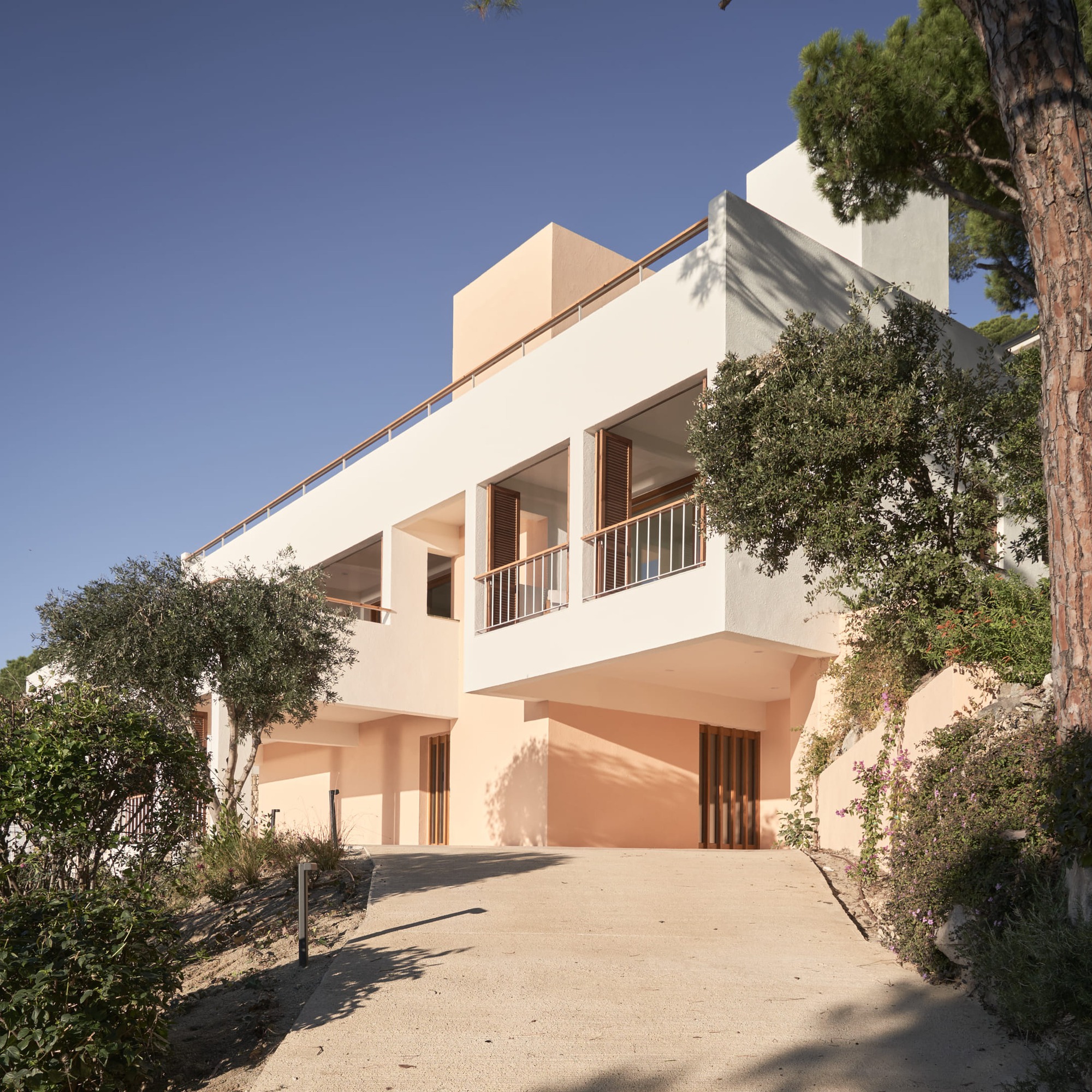 Sloped driveway approach to stucco facade with timber balcony and vertical slat screening