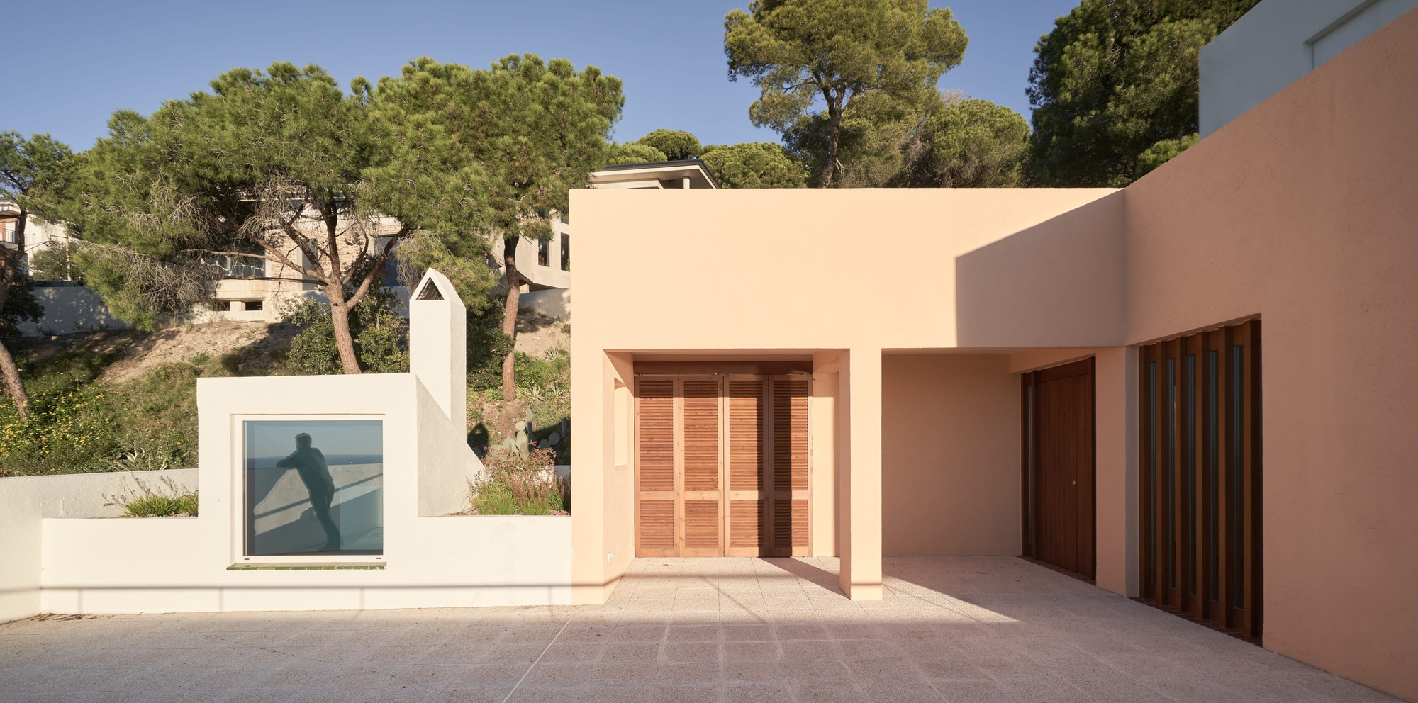 Terrace with timber door and vertical slat screen beside framed window with hillside trees beyond
