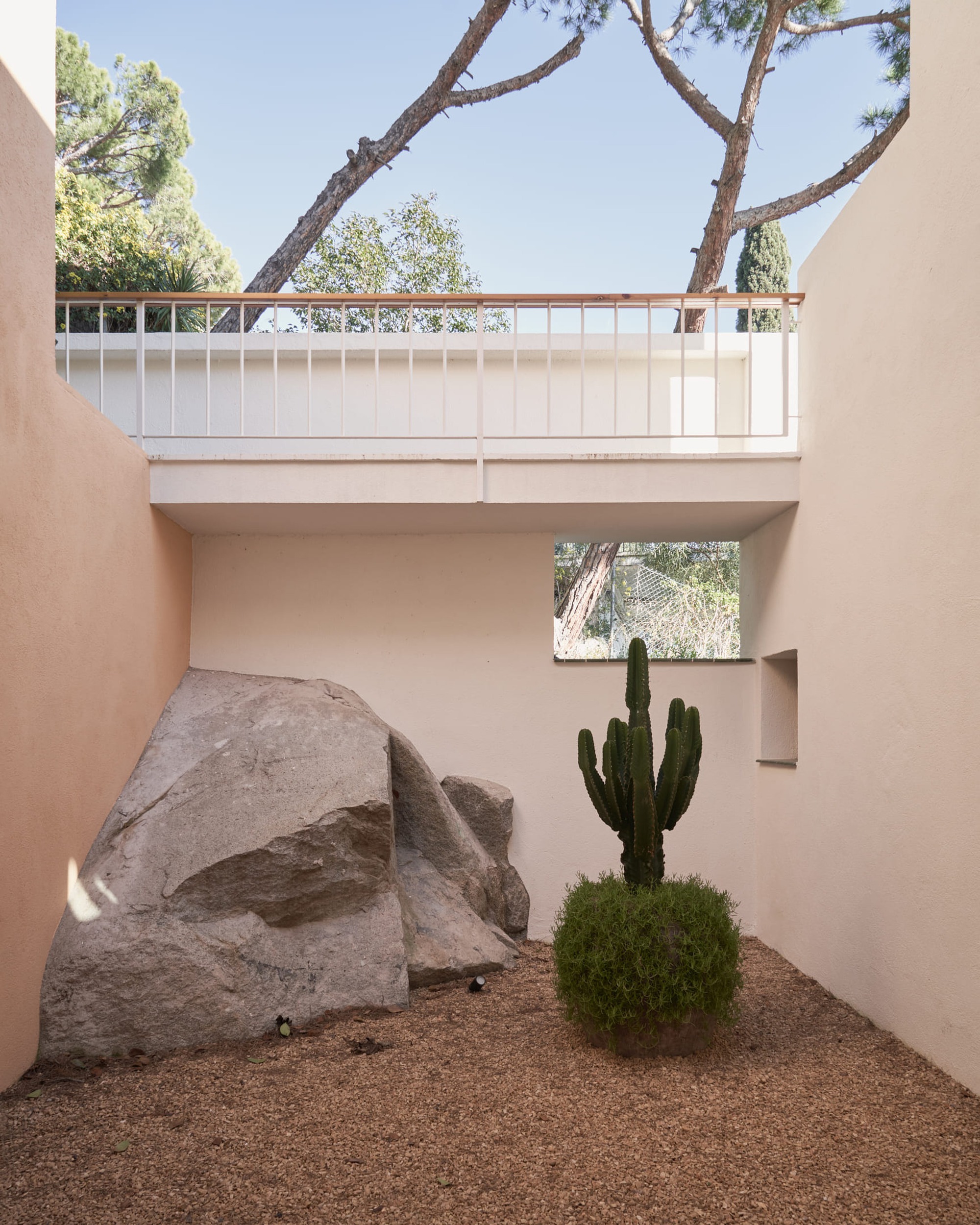 Courtyard with large boulder and cactus beneath a white metal railing balcony and pine trees