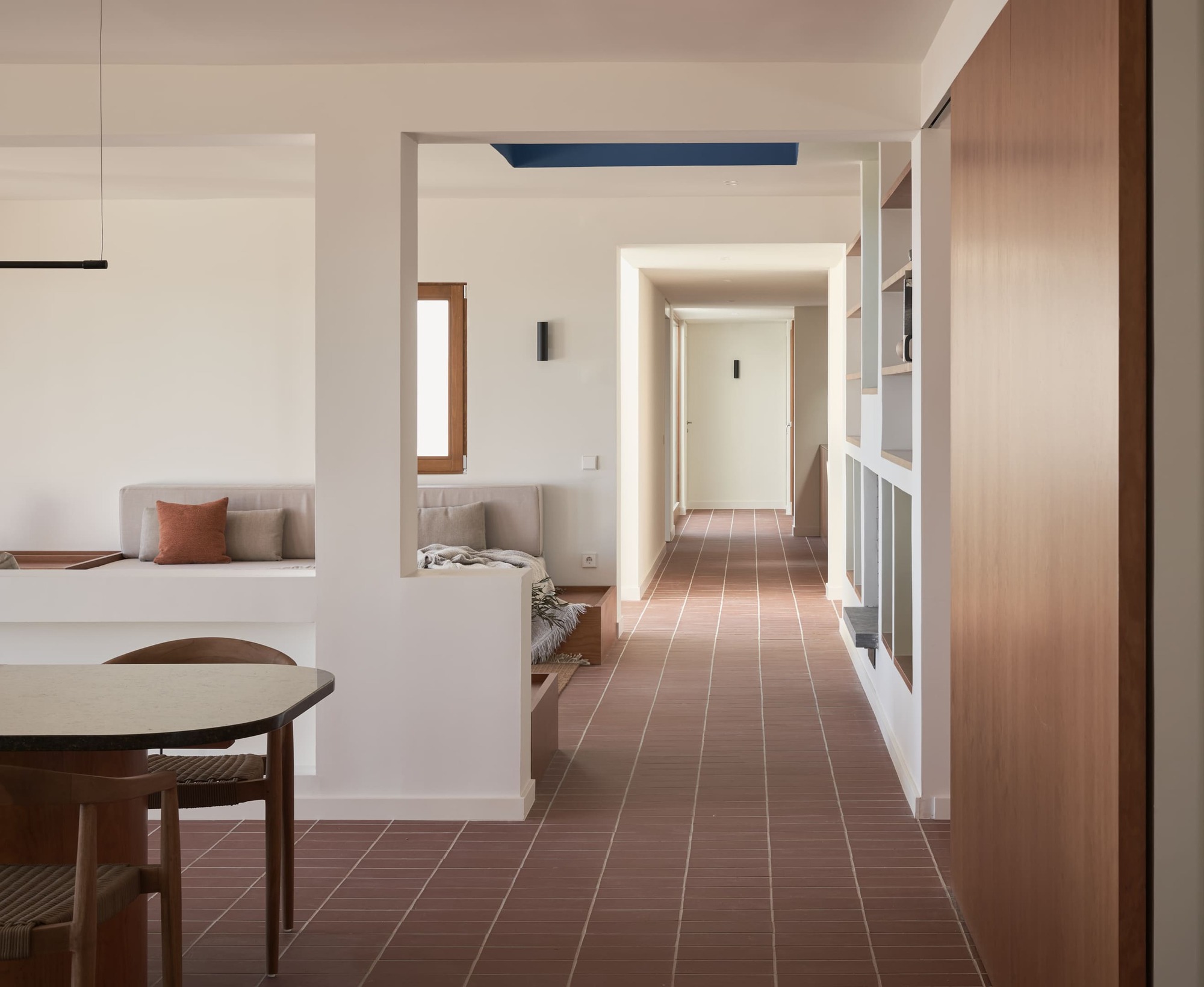 Corridor with terracotta tile floor leading past built-in seating nooks and timber millwork