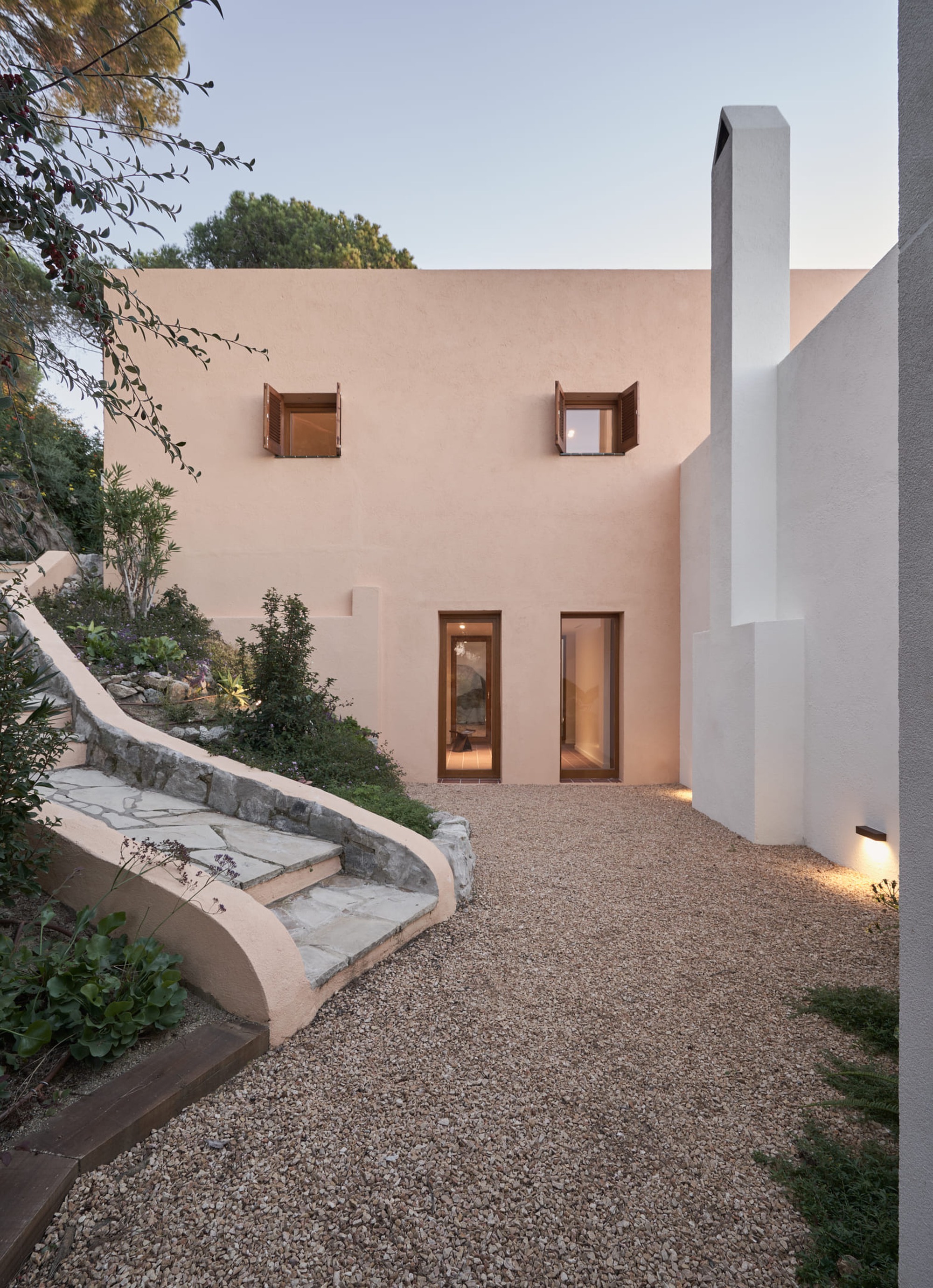 Gravel courtyard with curved stone steps leading to timber-framed windows lit at dusk