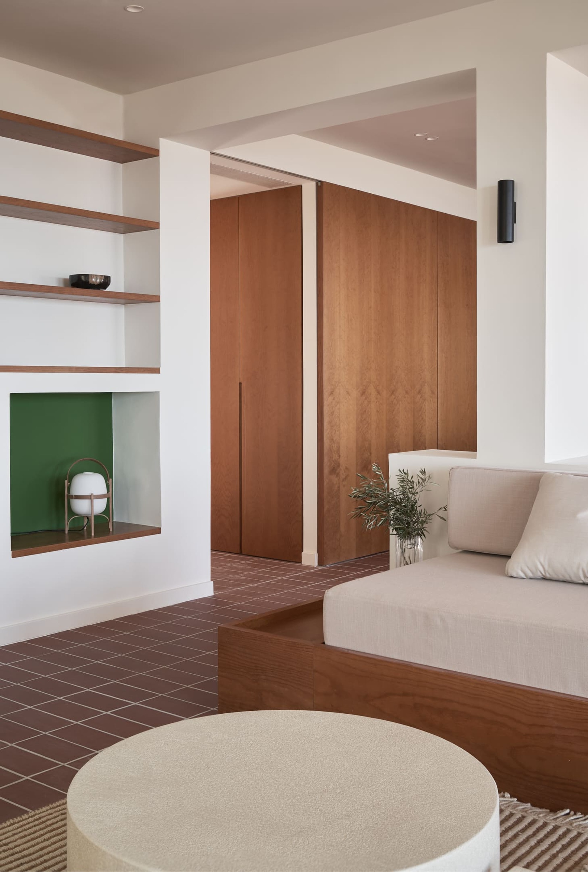 Built-in timber wardrobe with vertical grain panels beside open shelving with green-backed niche and terracotta flooring
