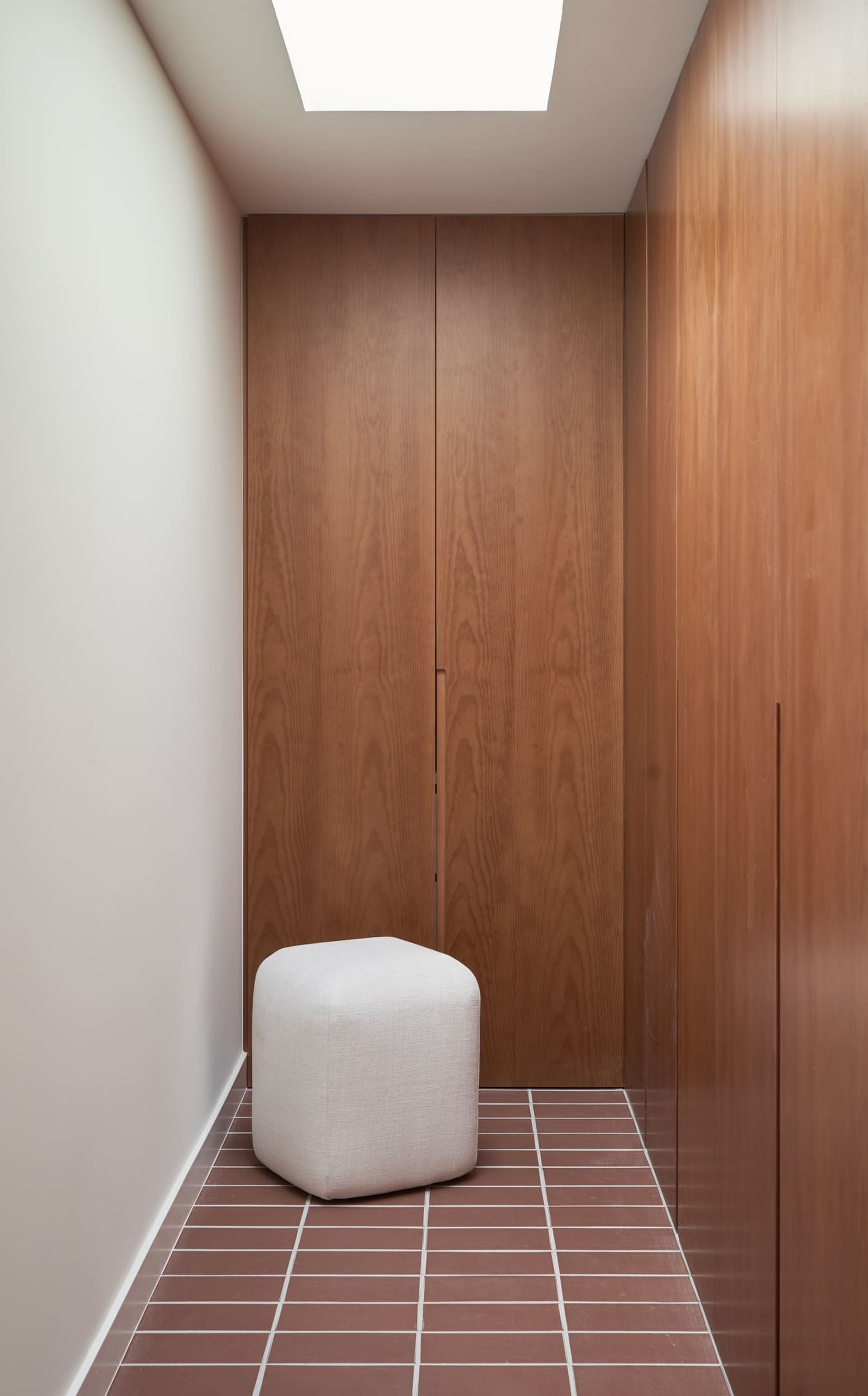 Narrow corridor with wood-paneled walls, terracotta square tile floor, and rectangular skylight overhead
