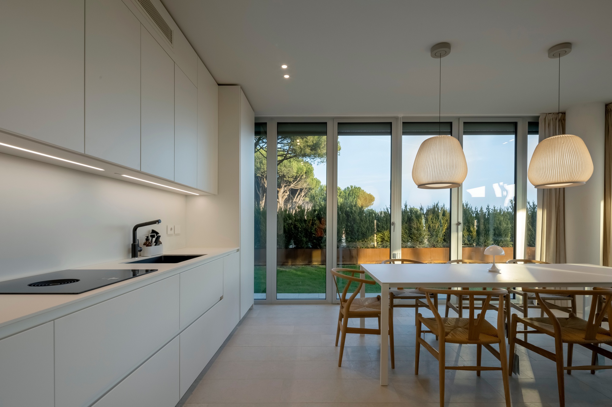 Open-plan kitchen and dining area with full-height glazing opening to a garden at dusk