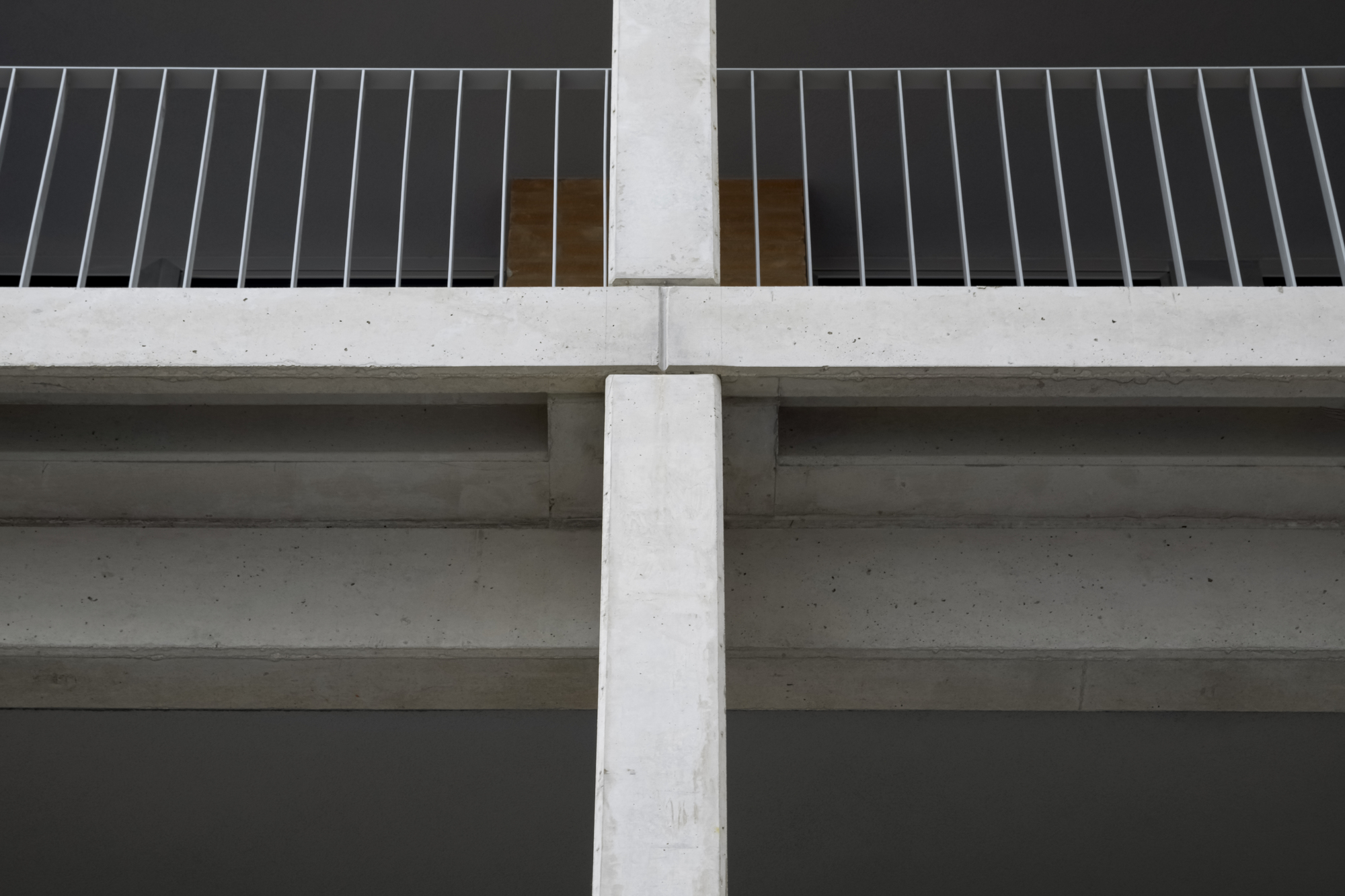 Underside view of concrete balcony slabs meeting a vertical column with vertical metal slat railing above