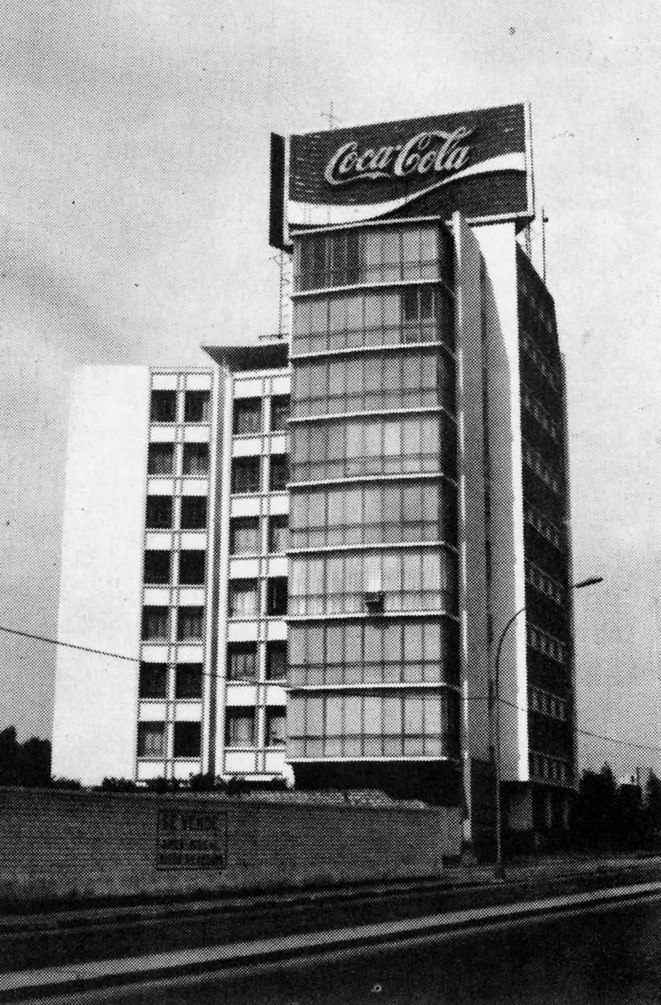 Corner view of the tower with horizontal bands of windows beneath a rooftop billboard