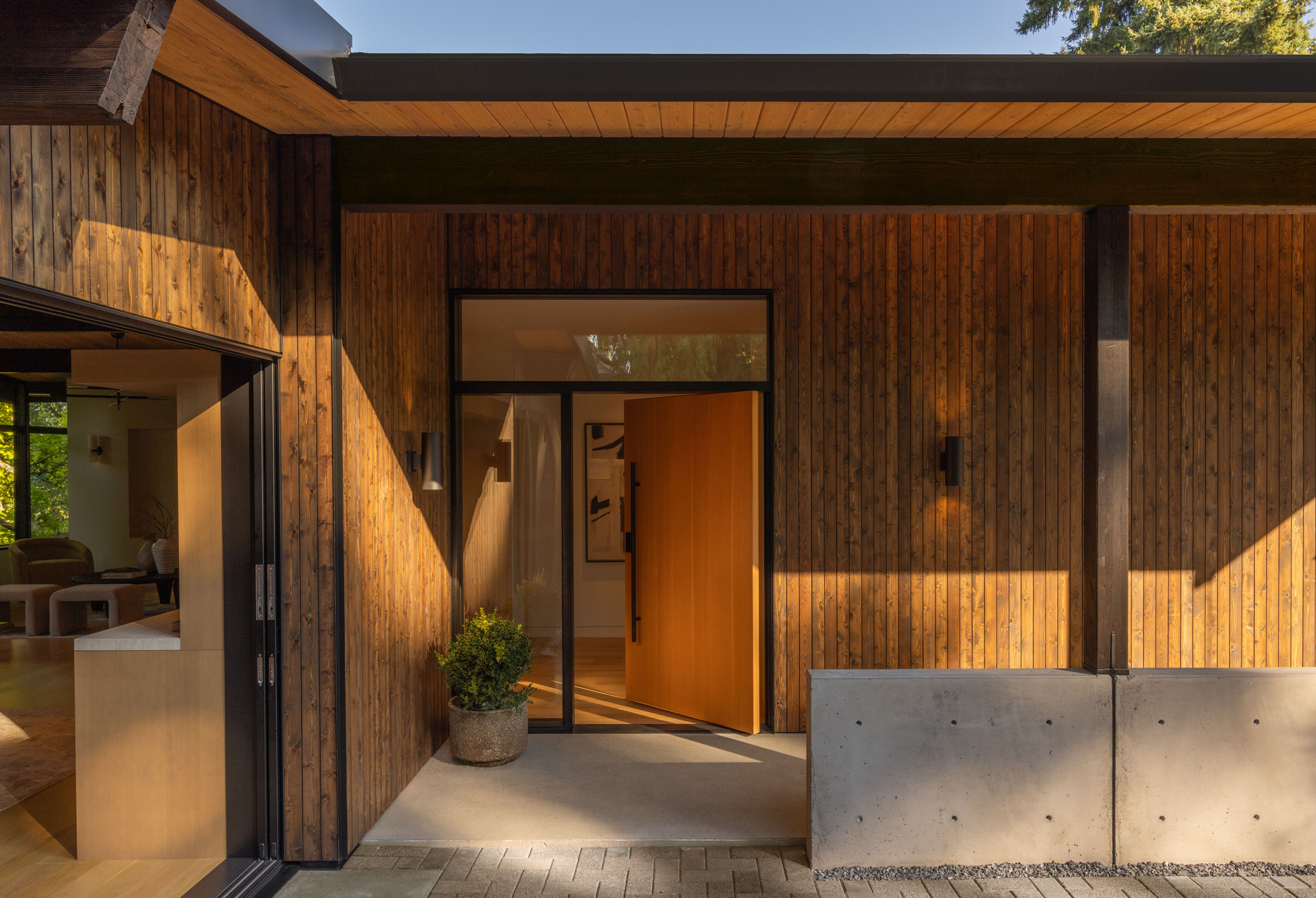 Glazed entrance door set in vertical timber cladding with warm interior light and concrete retaining wall
