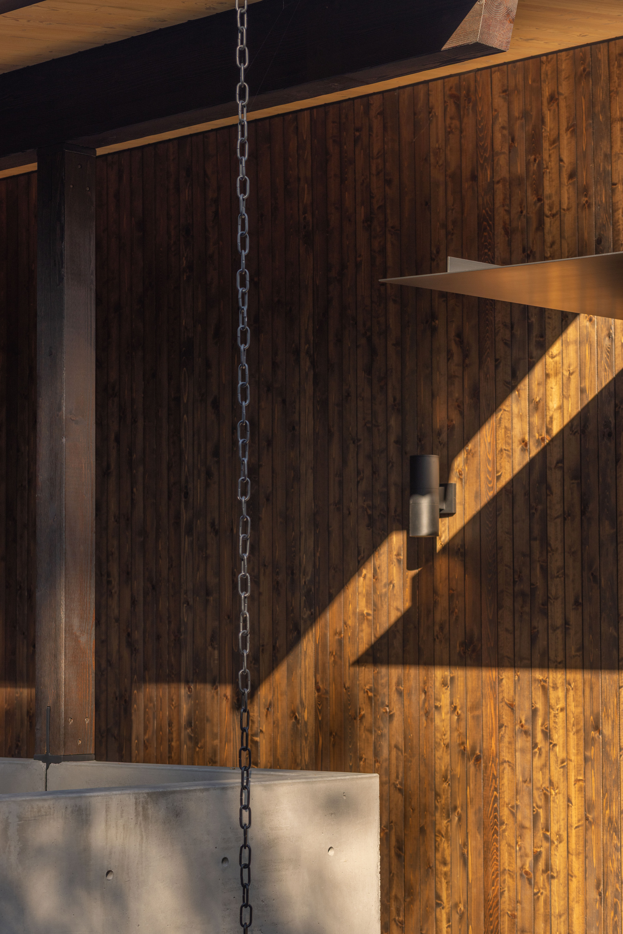 Vertical timber wall with suspended chain and diagonal shadow pattern in late afternoon light