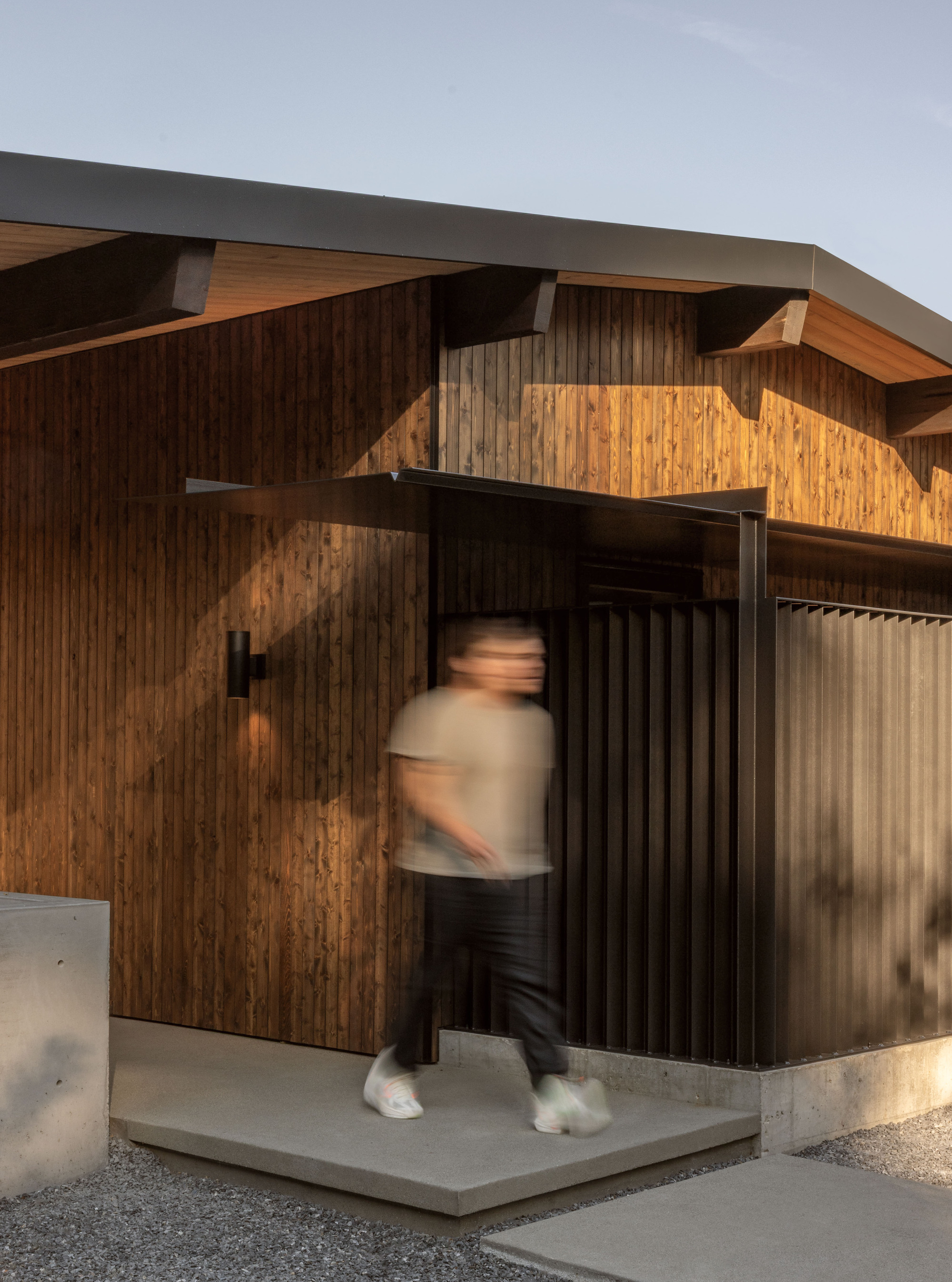 Entry threshold with vertical timber cladding and concrete base as a person moves through the doorway
