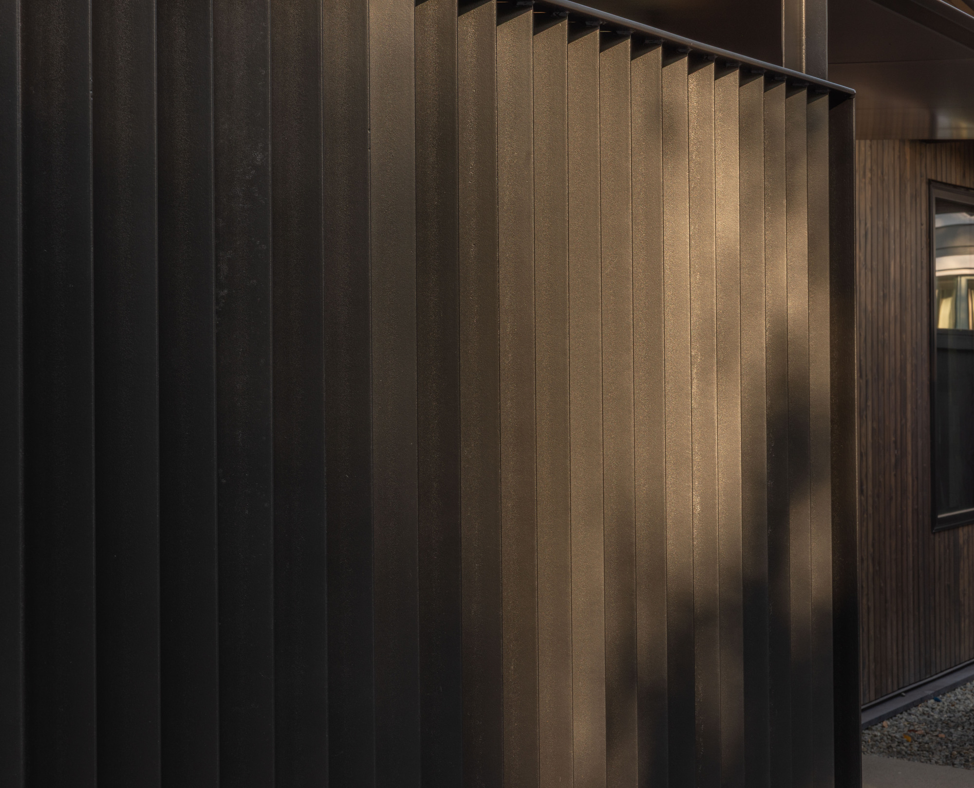 Close-up of vertical dark metal screening with light filtering through the slats at dusk