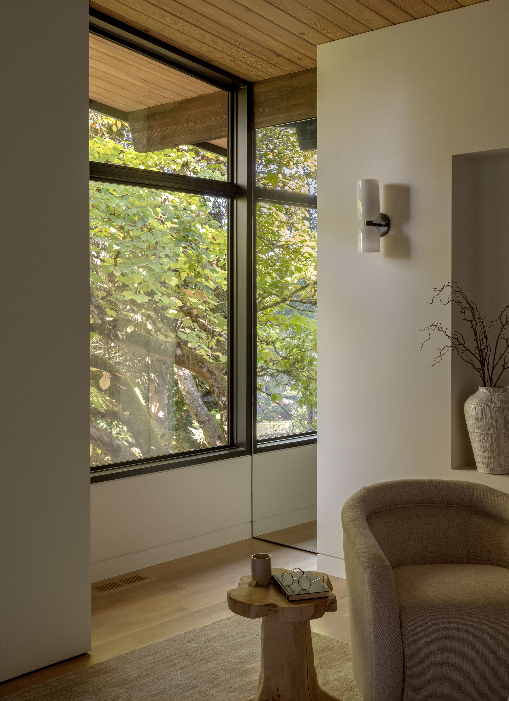 Corner seating area with timber ceiling and black-framed windows overlooking green summer foliage