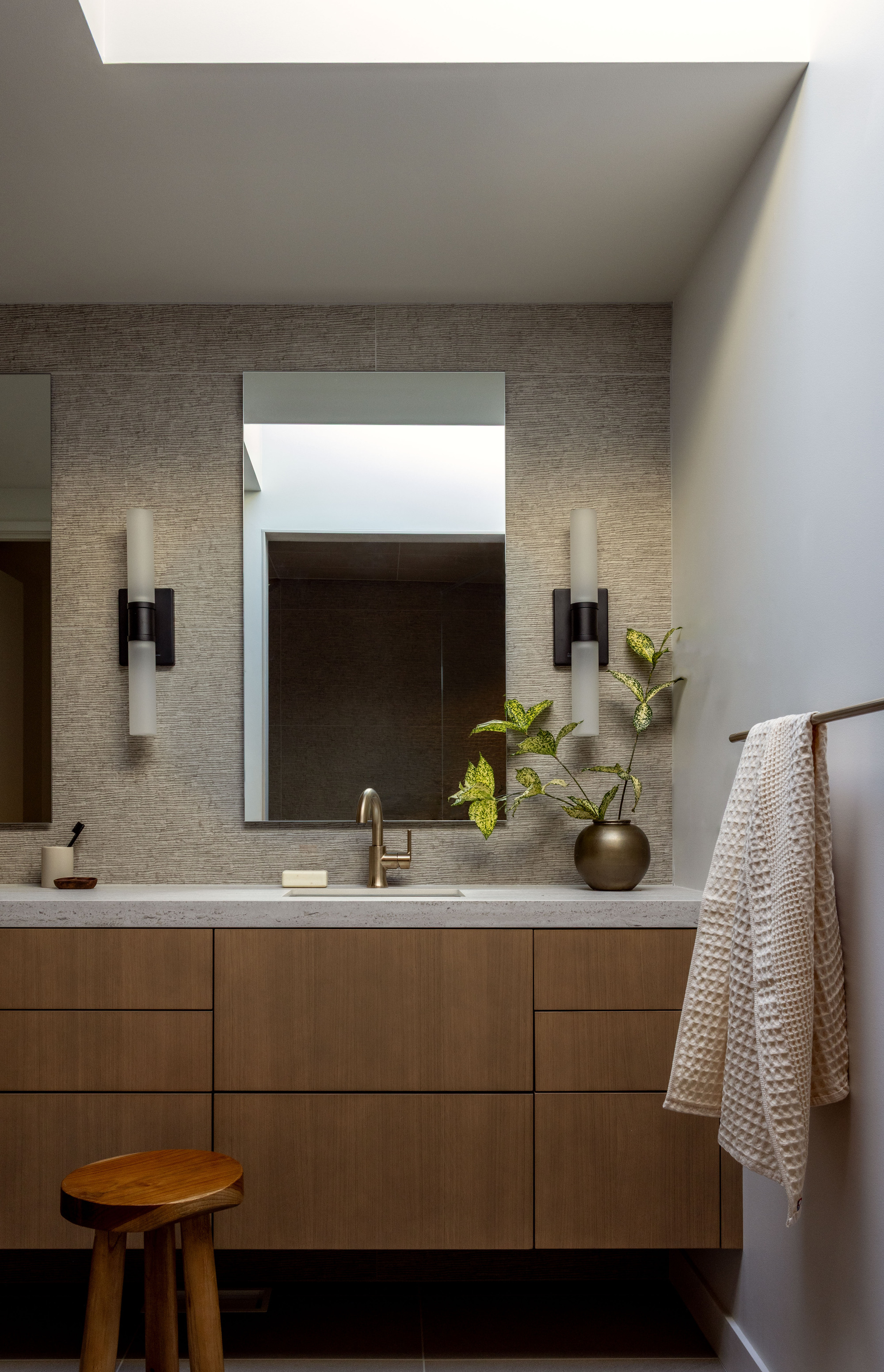 Bathroom vanity with walnut cabinetry, textured wall tile, and skylight above the mirror