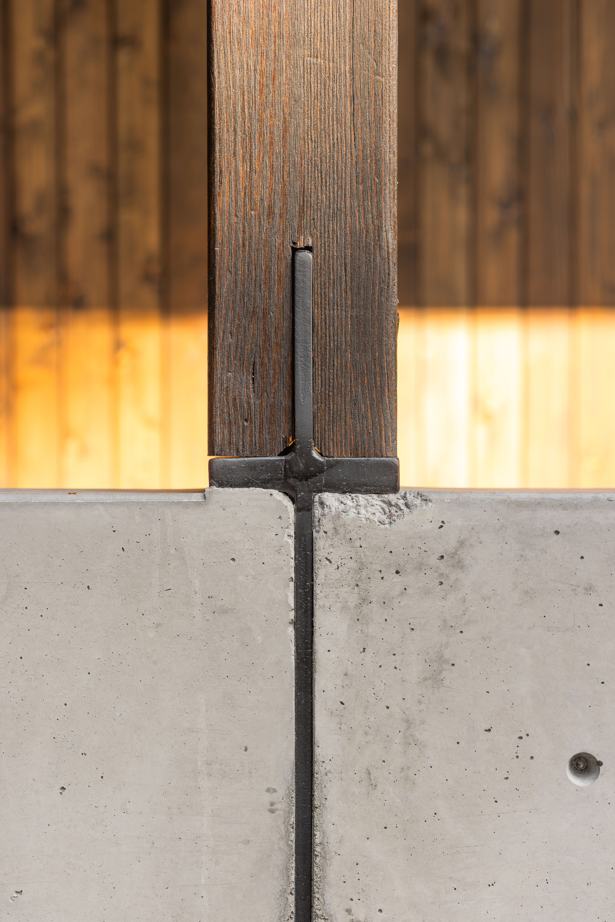 Detail of steel anchor plate connecting charred timber post to concrete foundation wall
