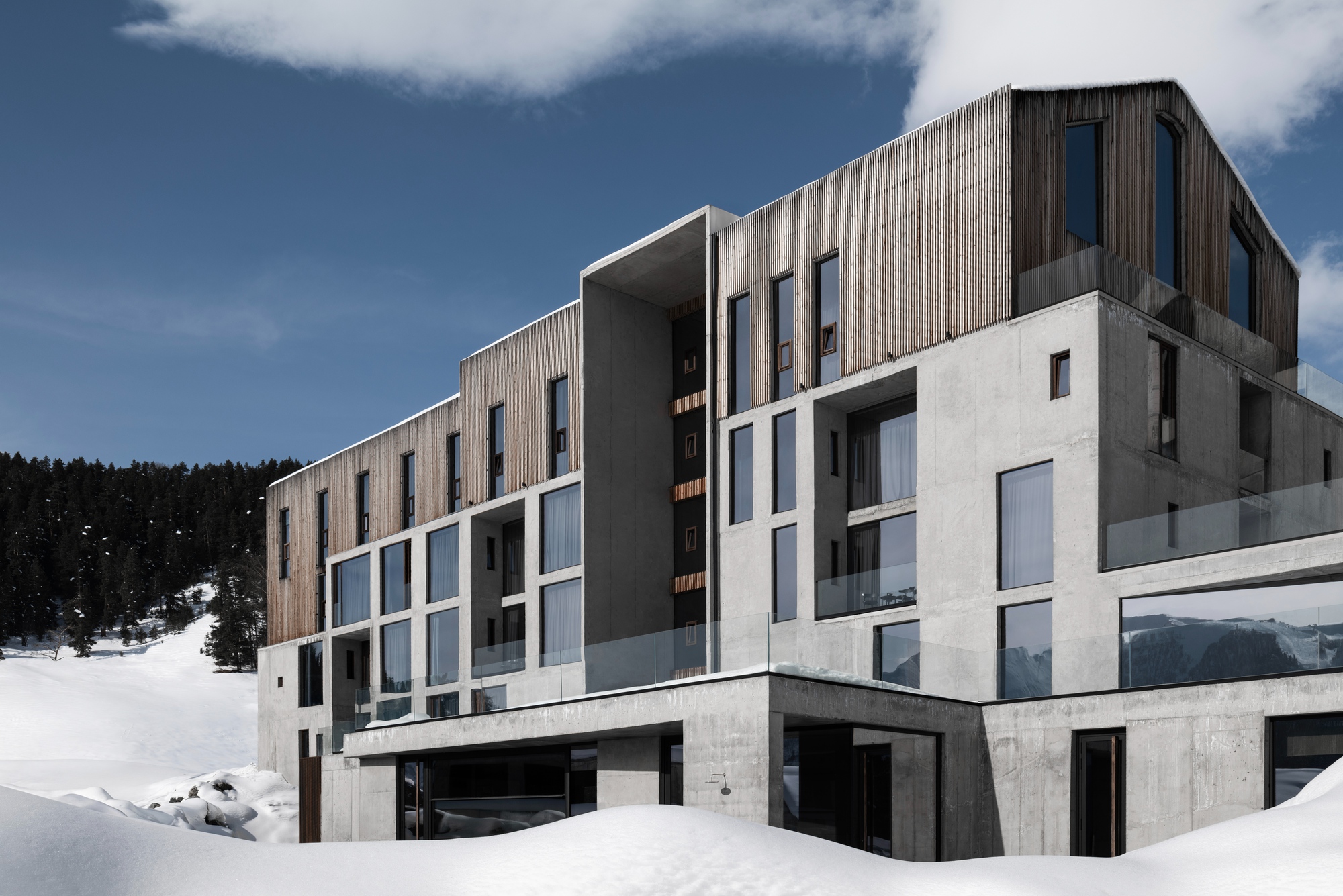 Layered facade combining timber cladding, concrete panels and glazing set into a snowy hillside