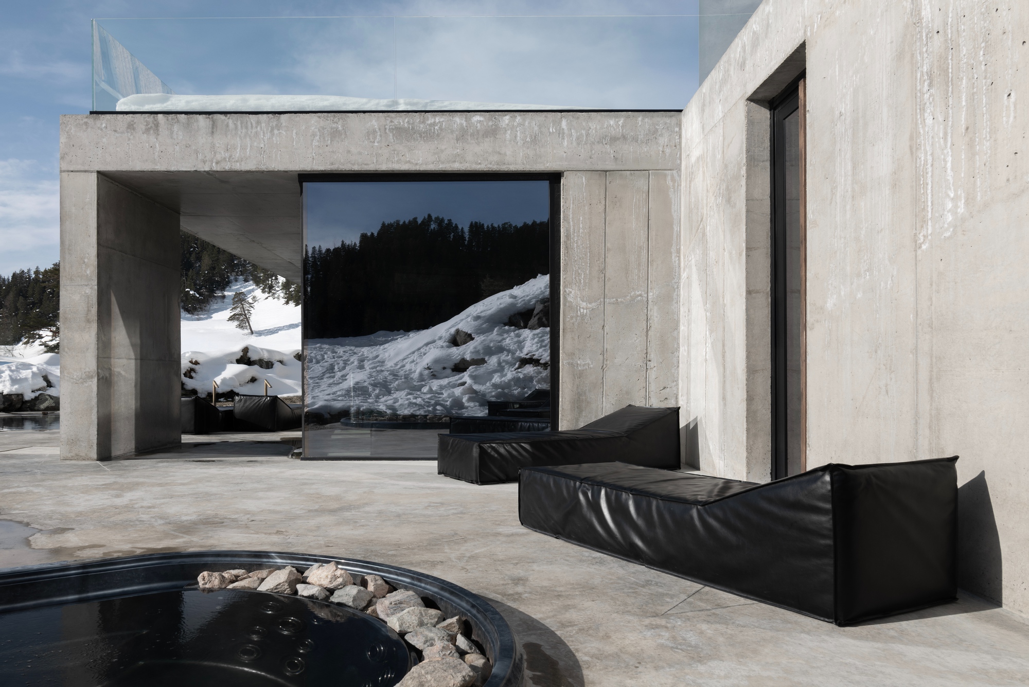 Concrete terrace with black leather seating and circular hot tub overlooking a winter landscape