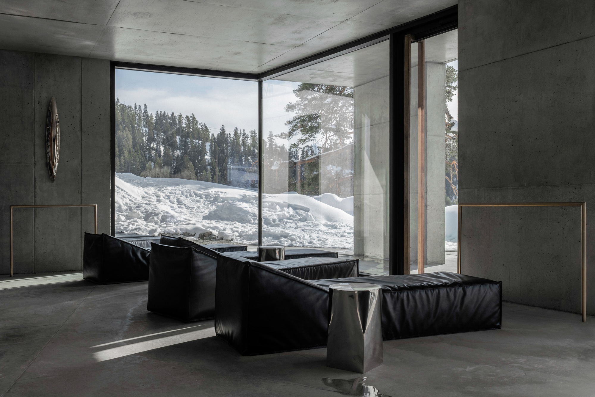 Lounge area with corner glazing framing snow-covered slopes and low black seating on polished concrete floors