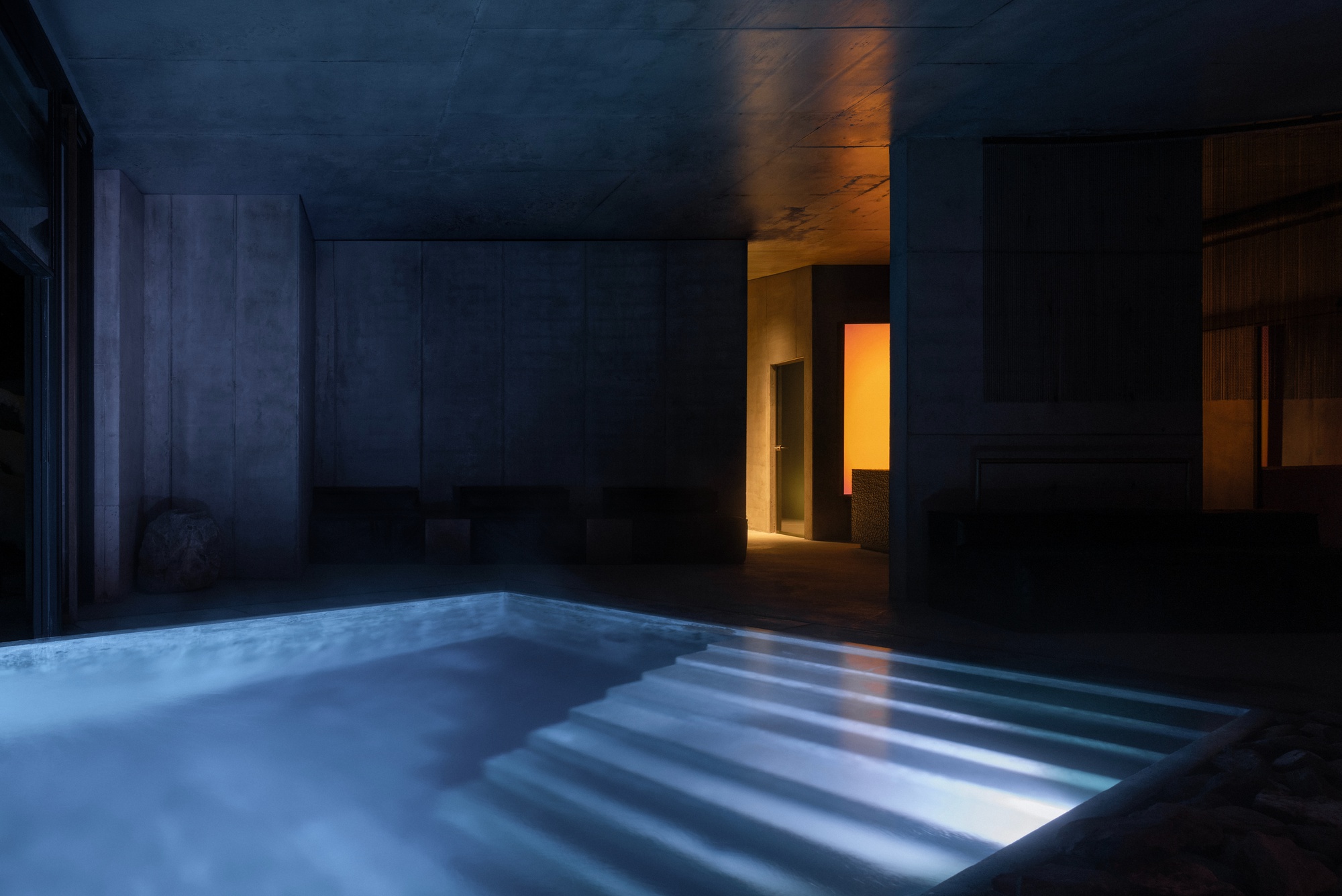 Indoor pool with illuminated water ripples and warm light spilling from a corridor at dusk