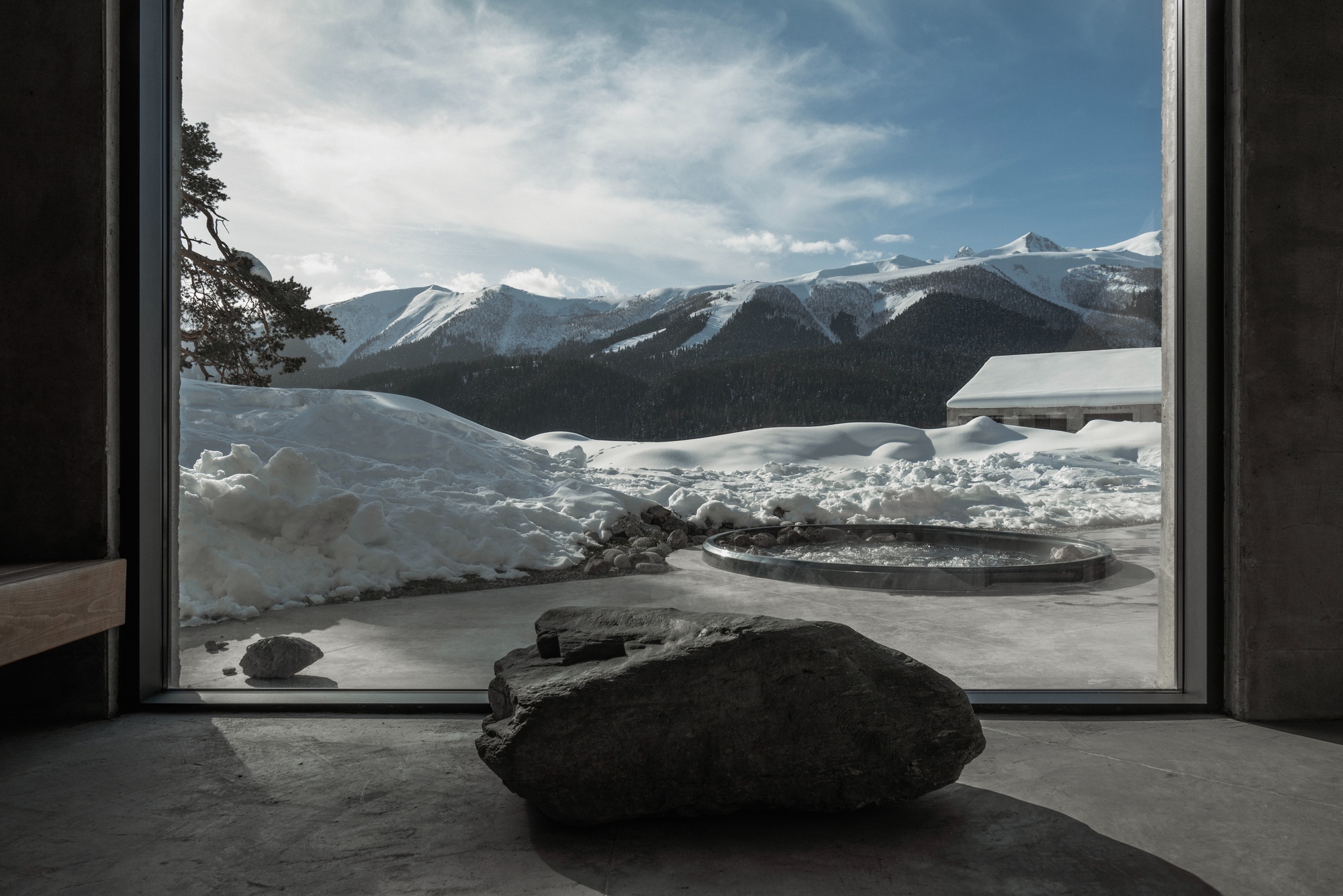 Floor-to-ceiling window framing a boulder on a concrete floor with snow-covered mountains beyond