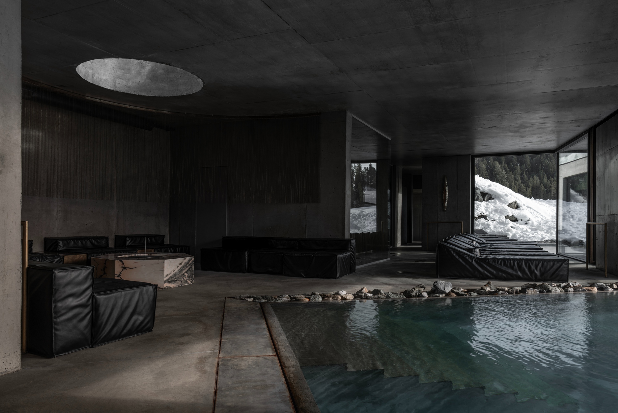 Indoor pool with dark timber walls and circular ceiling skylight overlooking snowy landscape