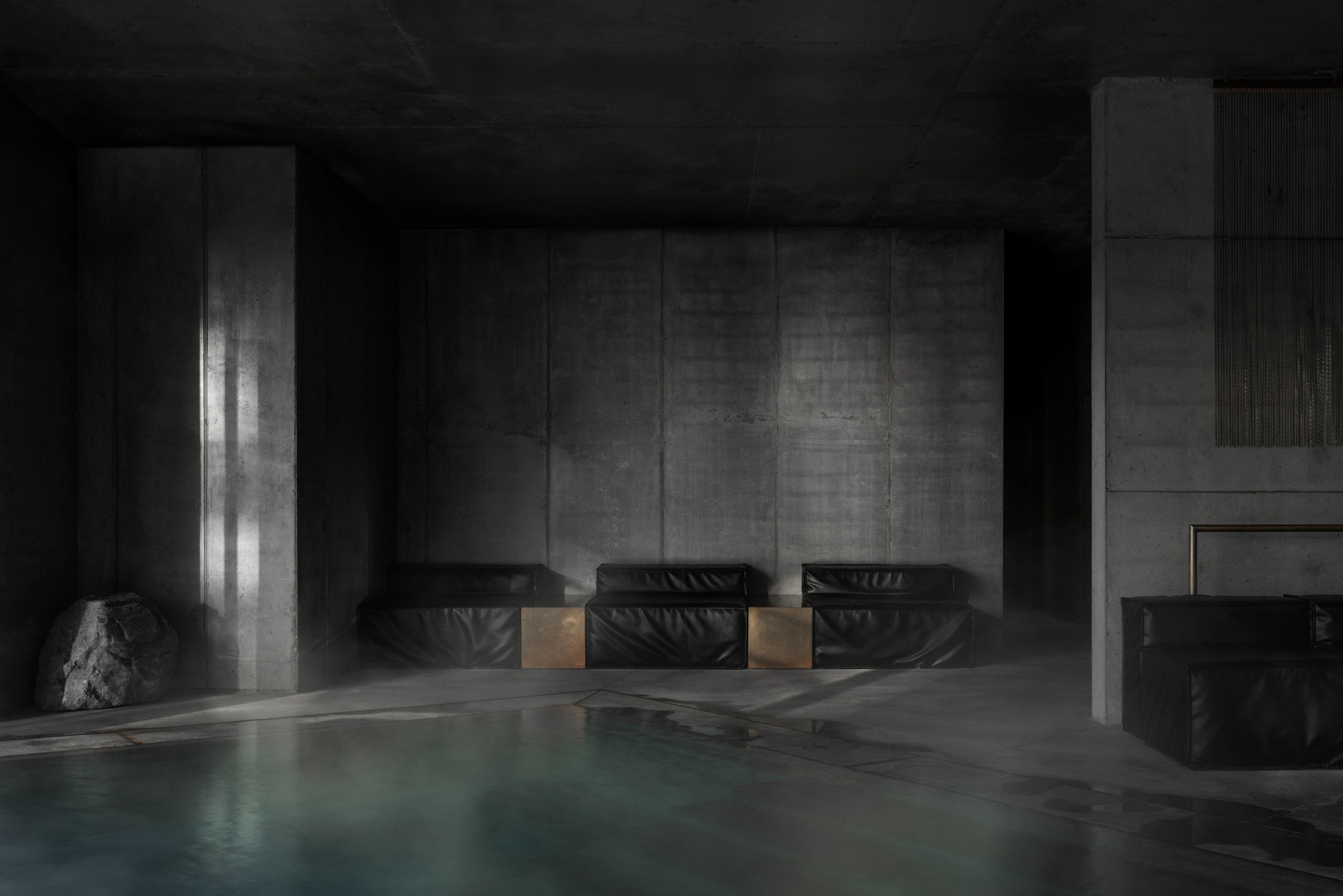 Three black leather lounge chairs against concrete wall beside pool edge with dramatic side lighting