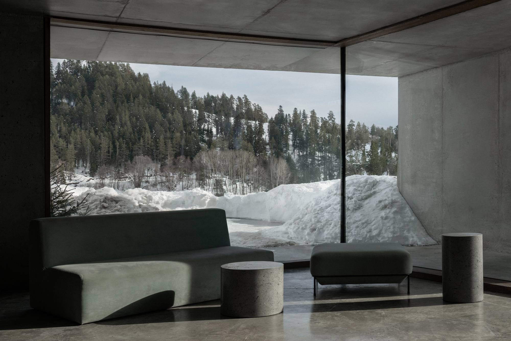 Corner window overlooking forested hillside with snowbanks and concrete seating elements in foreground