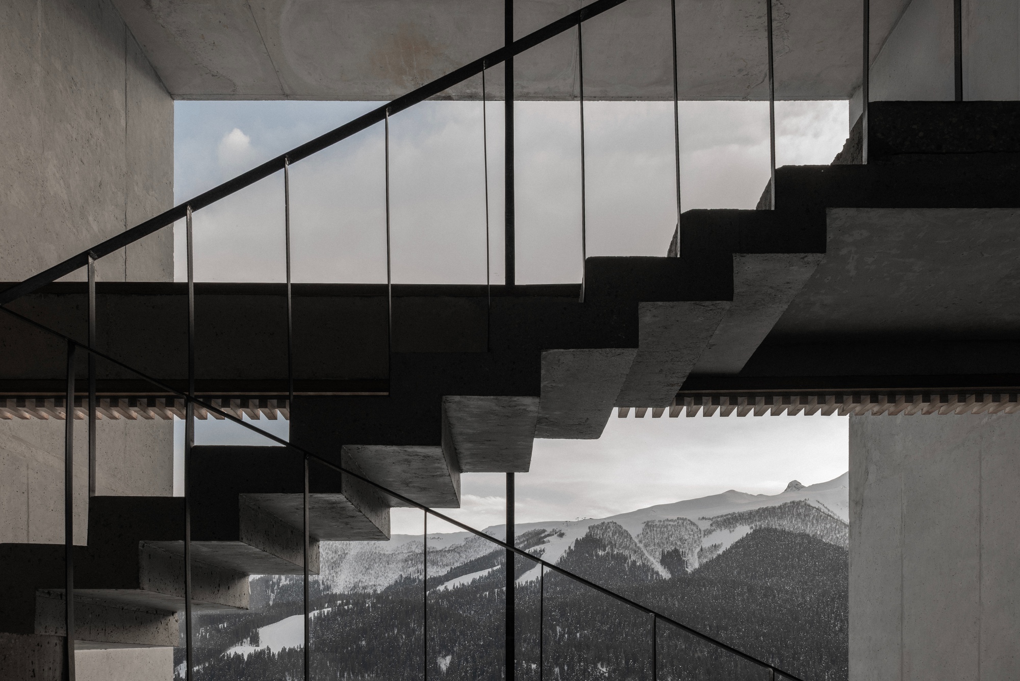 Steel and glass staircase ascending past concrete walls with framed mountain view beyond