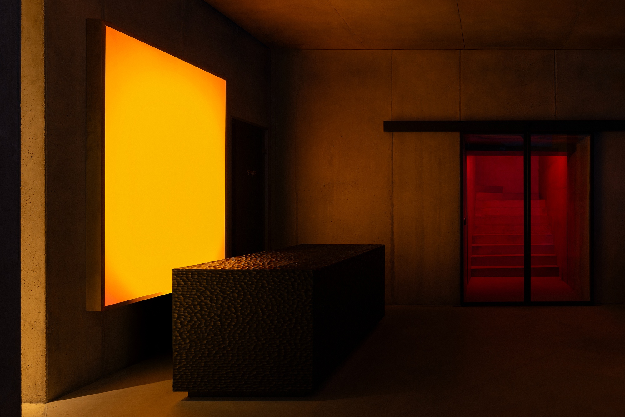 Interior wellness area with amber backlit panel and red-lit sauna chamber beside textured stone wall