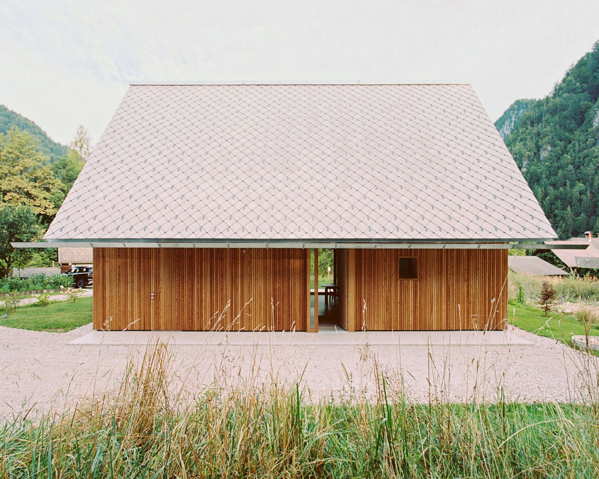 Front elevation showing vertical timber cladding beneath a diamond-patterned shingle roof with mountains behind