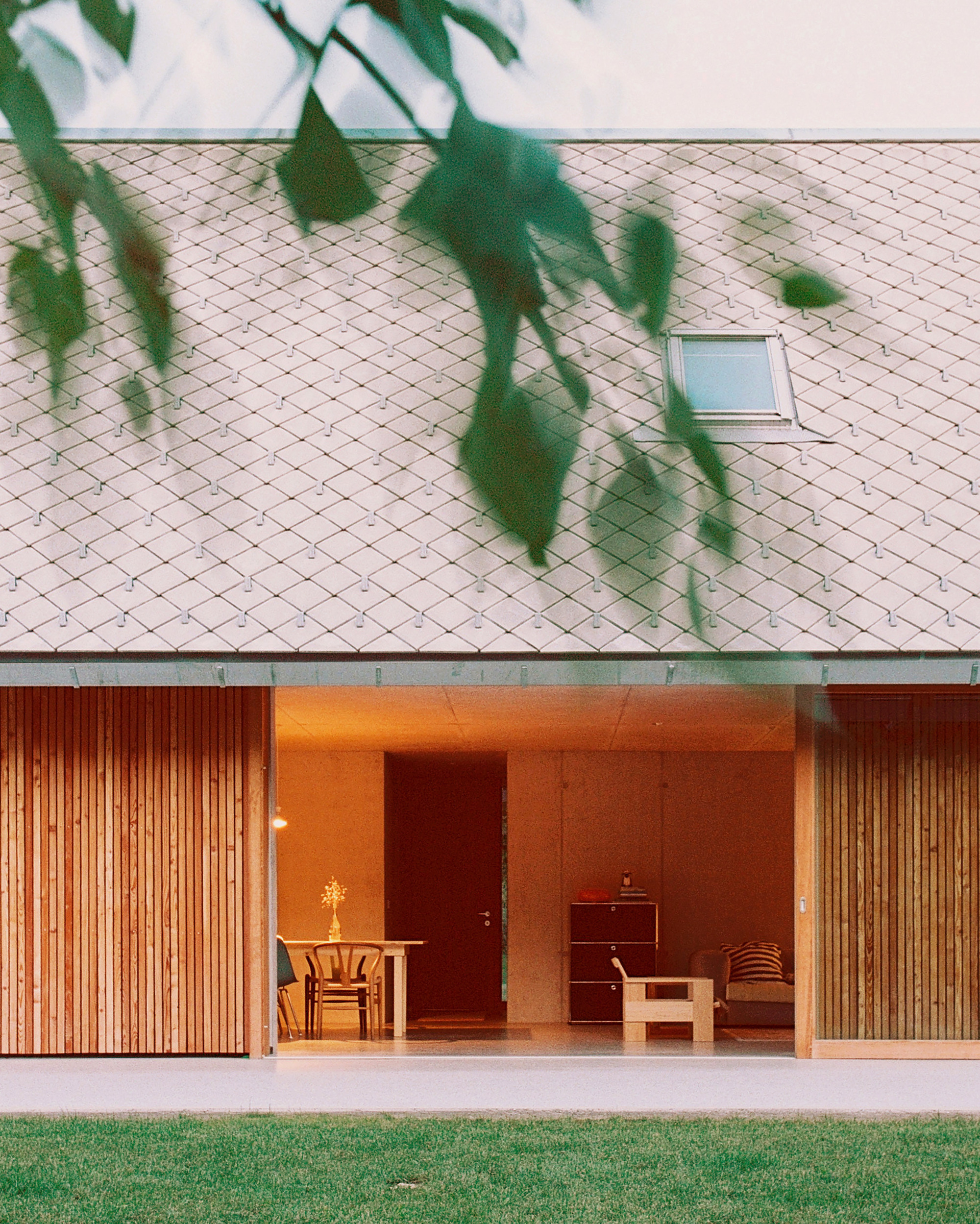 Covered porch with timber slat screens, red-painted wall, and tree shadows cast across the shingle roof
