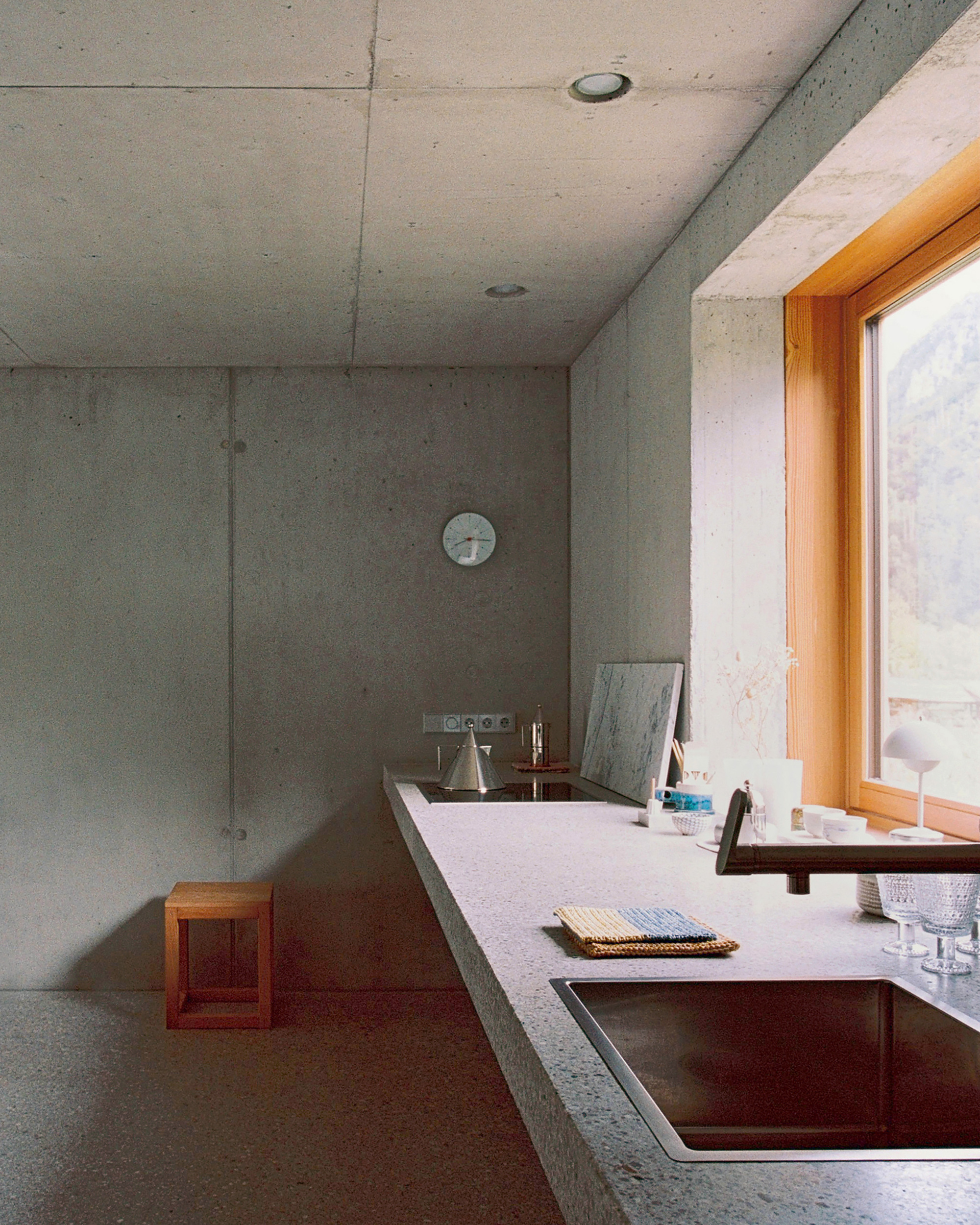 Kitchen with board-formed concrete walls, terrazzo countertop and copper sink beneath a round wall clock