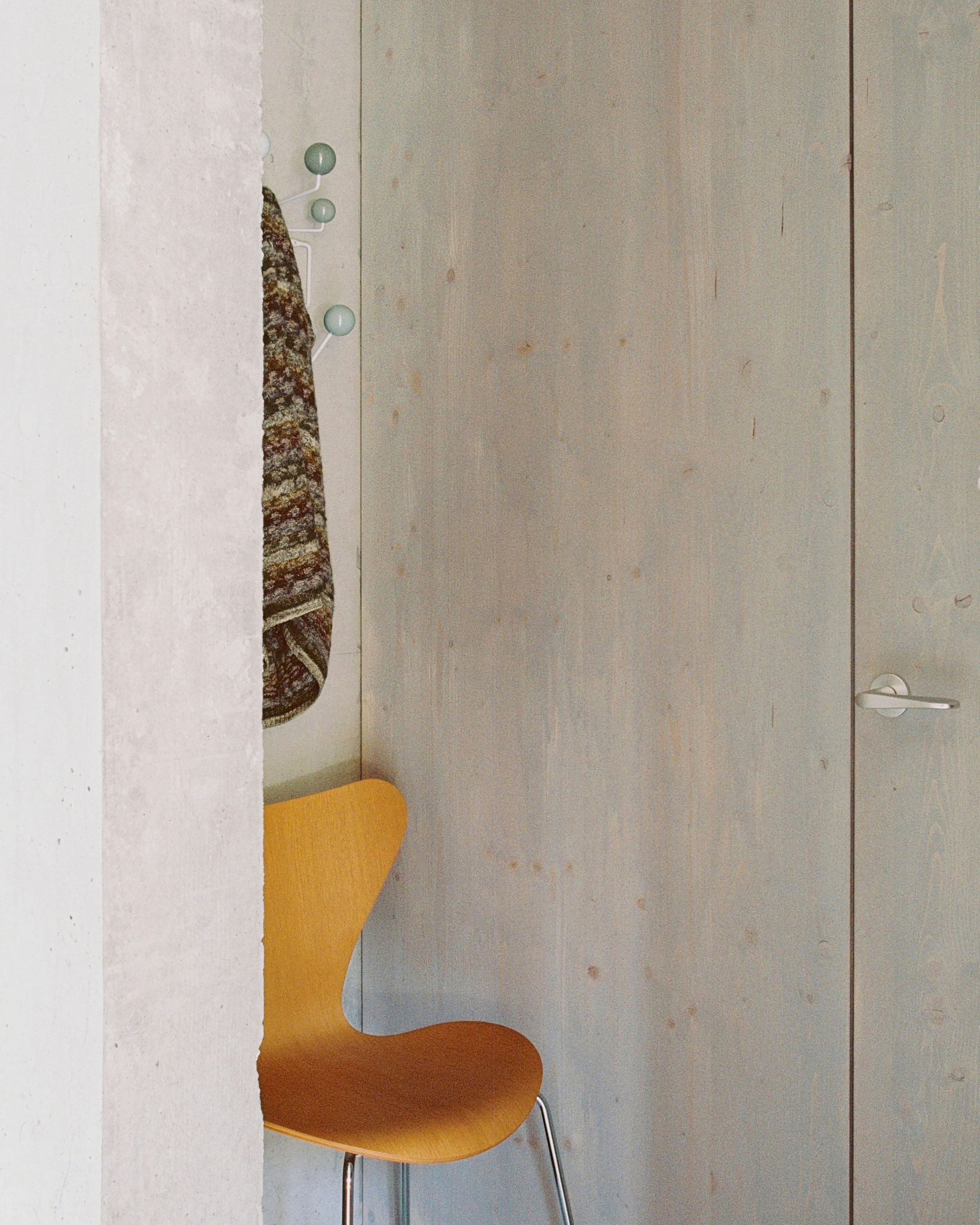 Detail of a plywood door slightly ajar with an orange upholstered chair visible through the opening