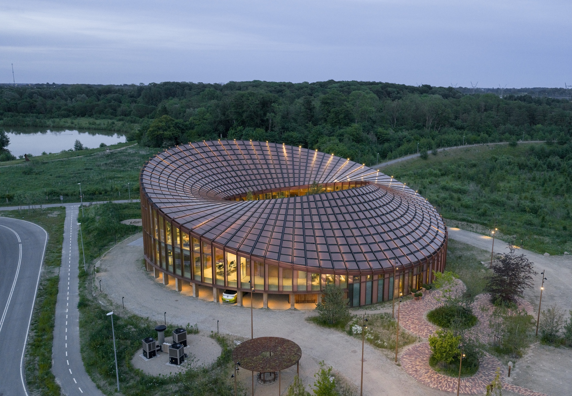 Aerial view of the circular building with spiraling tiled roof surrounded by parkland at dusk