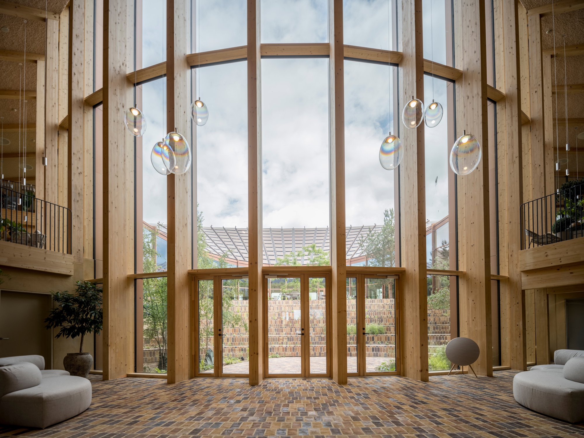 Double-height glazed timber frame entrance with suspended glass pendant lights and brick floor below